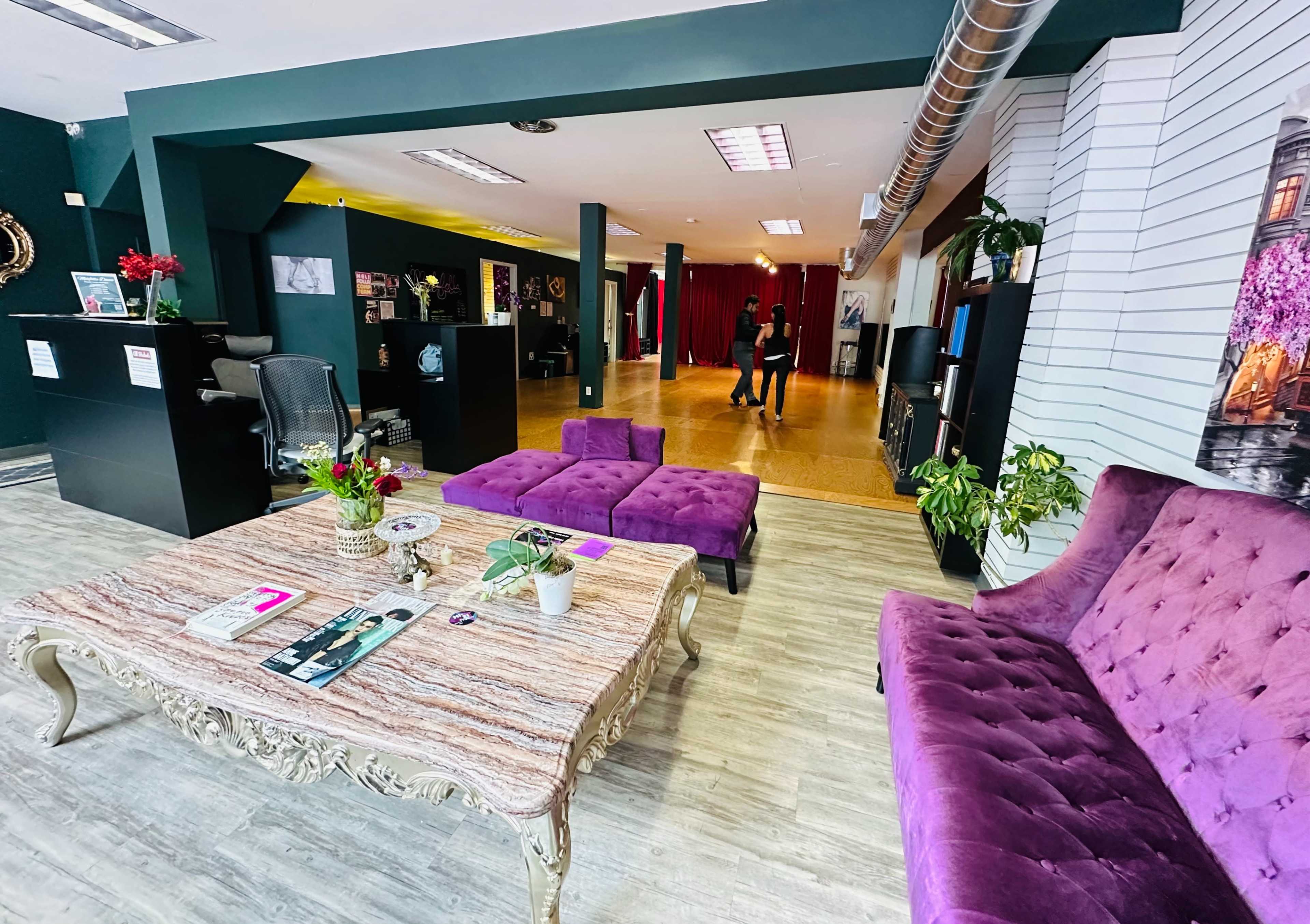 A lounge area with purple furniture, a decorative table, and an open space in the background where two people are interacting.