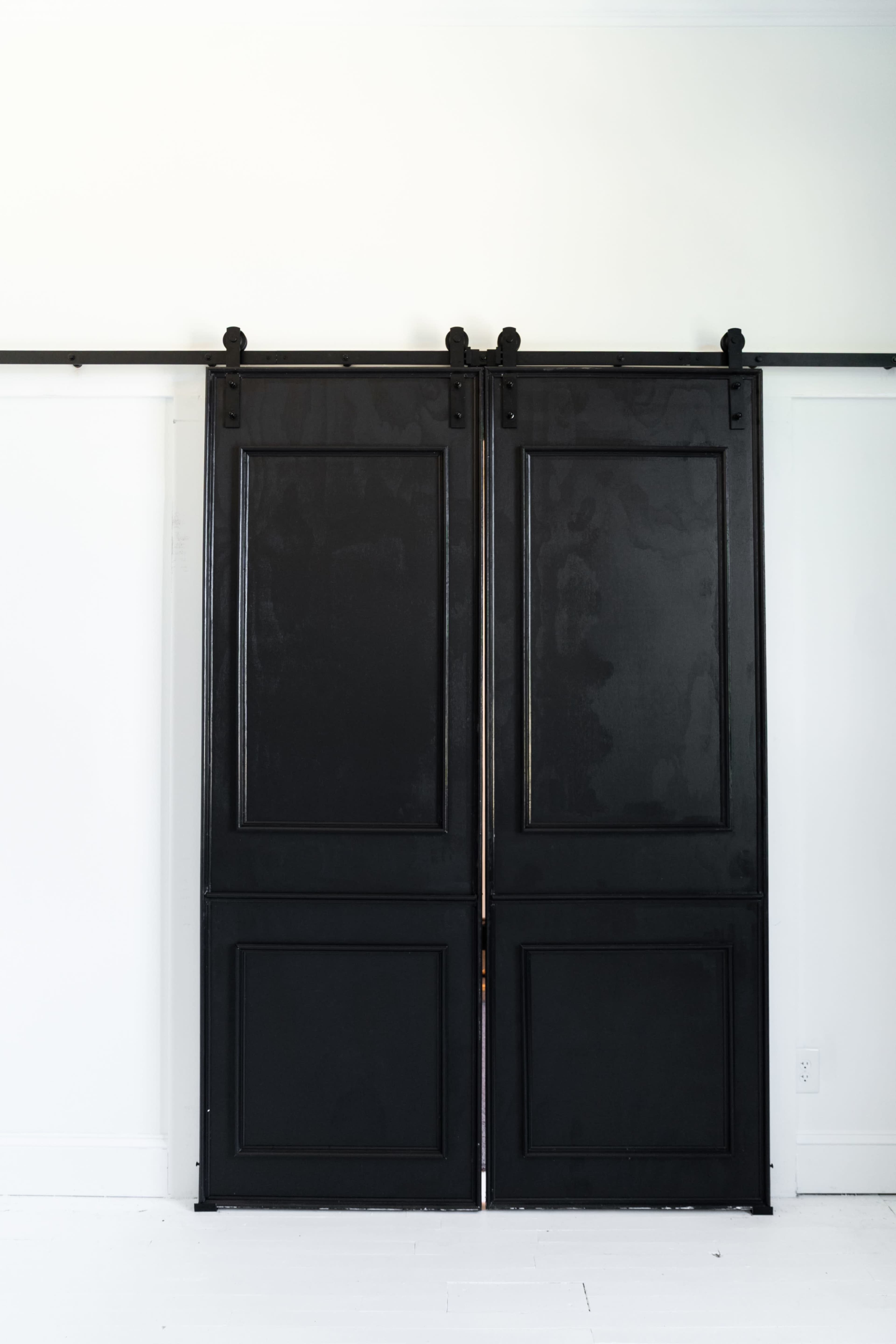 Two black sliding doors are positioned against a white wall, mounted on a metal track.