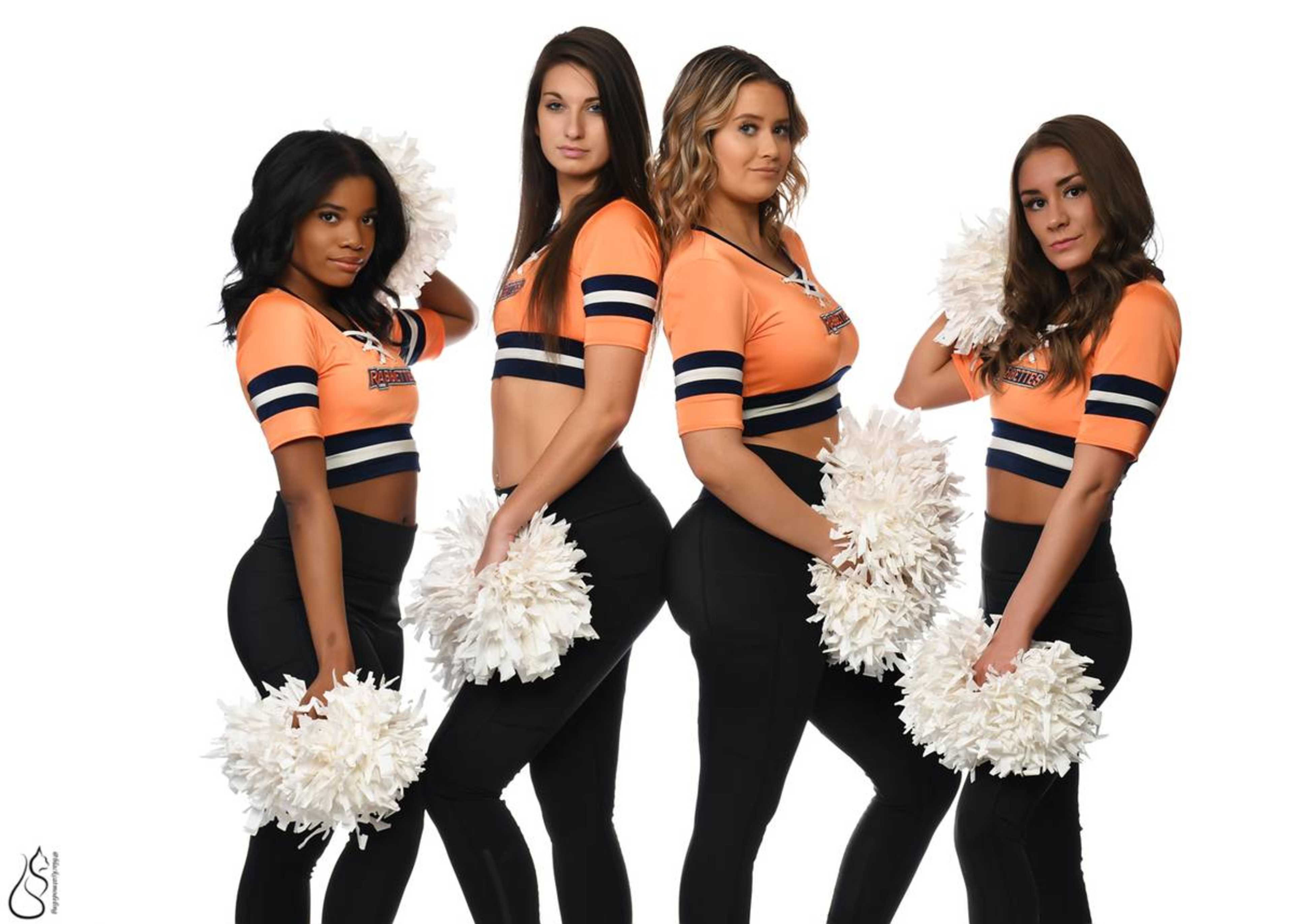 Four cheerleaders, dressed in matching orange and black uniforms, stand in a lineup holding white pom-poms.
