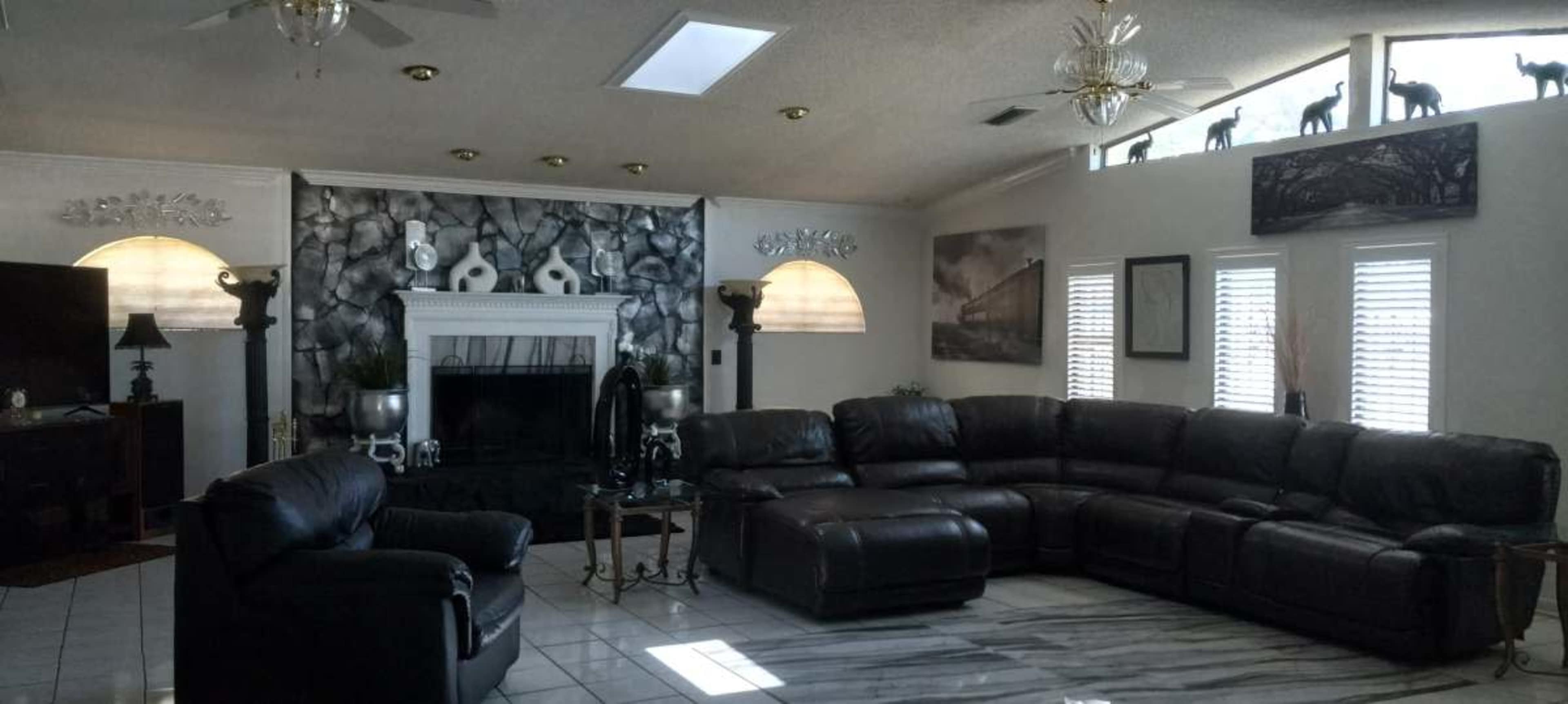 The image shows a spacious living room with a large sectional sofa, a fireplace, and decorative elements like wall art and sculptures.
