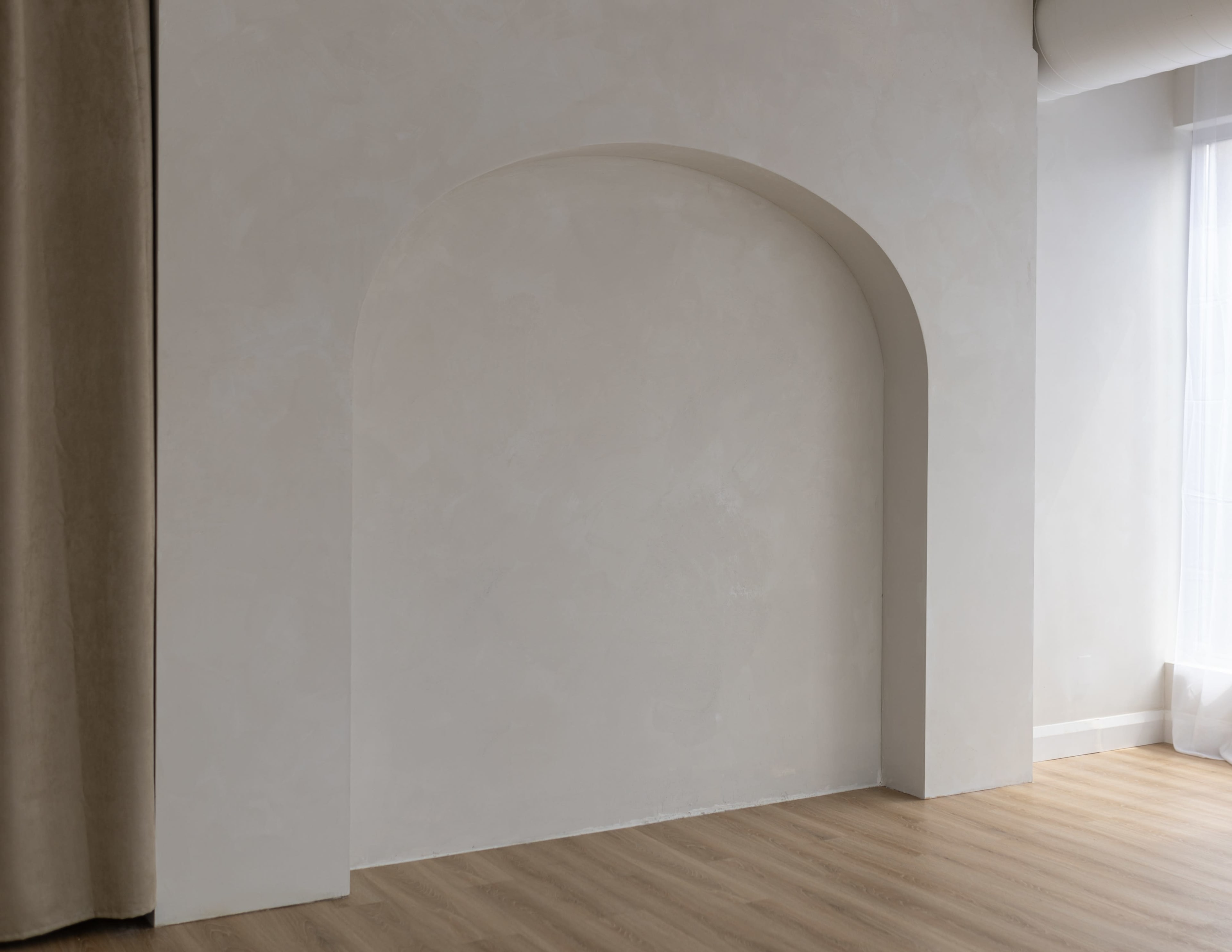 A simple room with a light-colored wall featuring a large arched recess and wooden flooring.