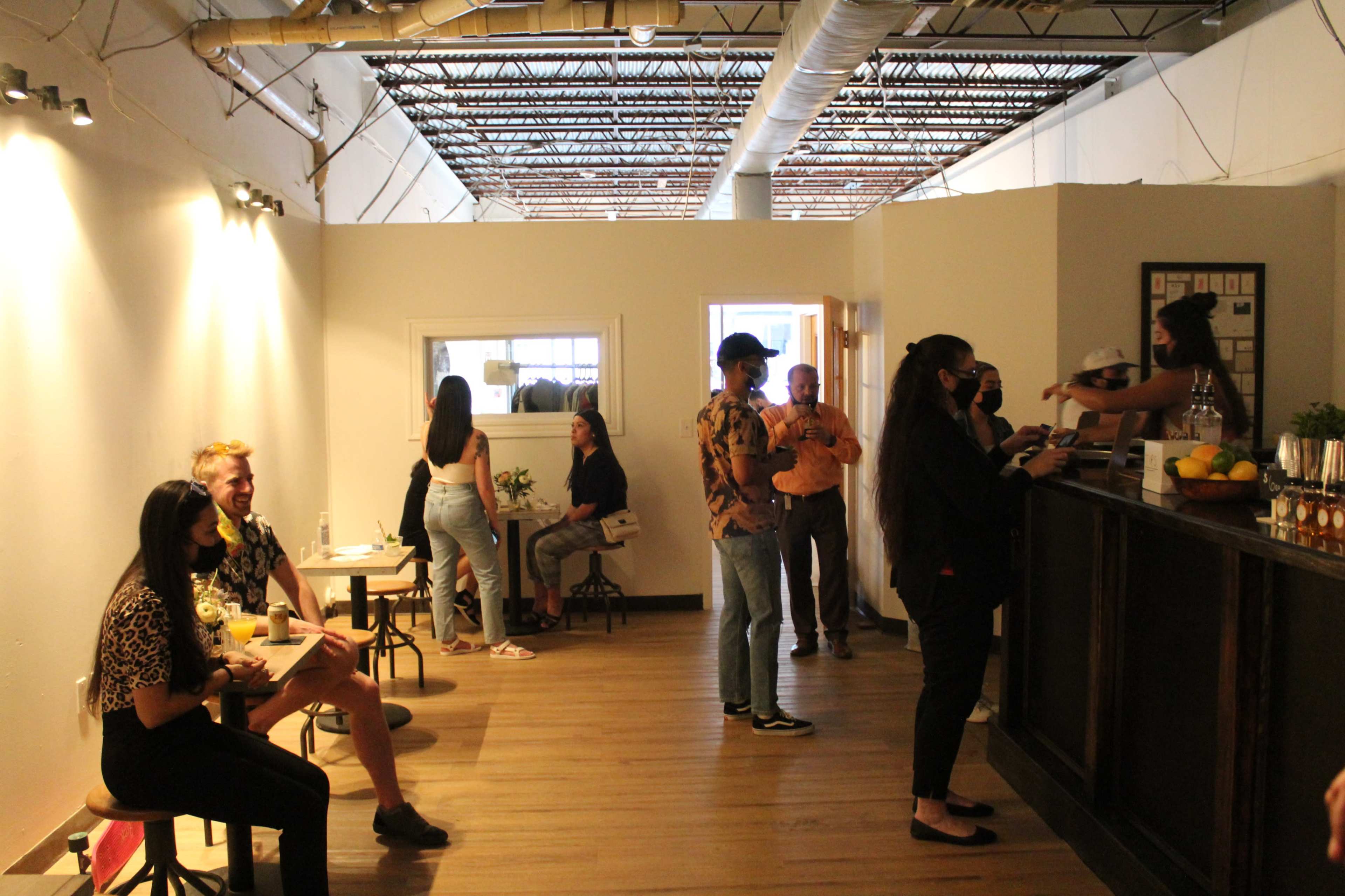 A group of people are seated at small tables and interacting with a staff member at a counter in a brightly lit café.