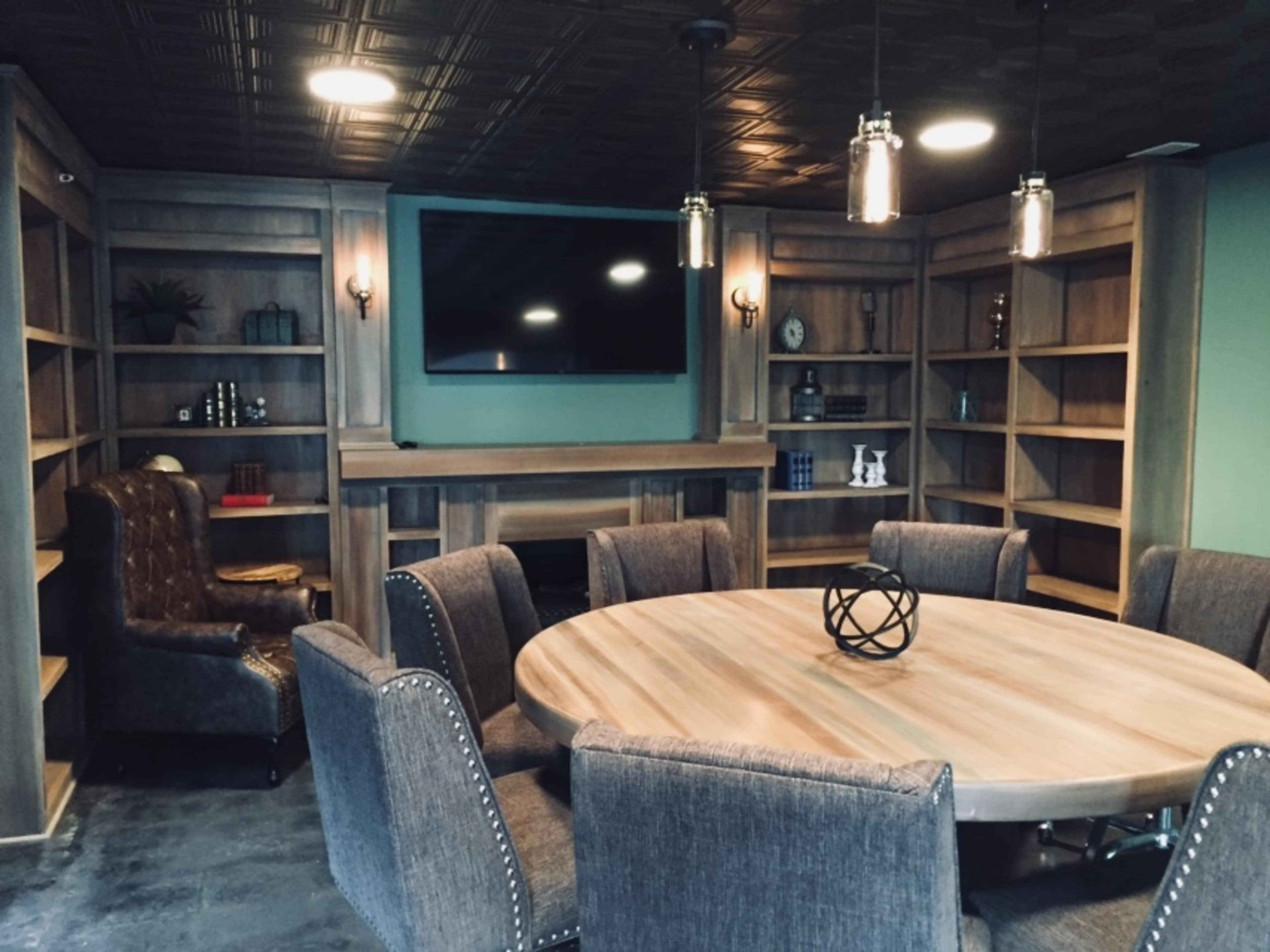 A cozy room featuring a round wooden table surrounded by upholstered chairs, with built-in wooden shelves and a television mounted on the wall.