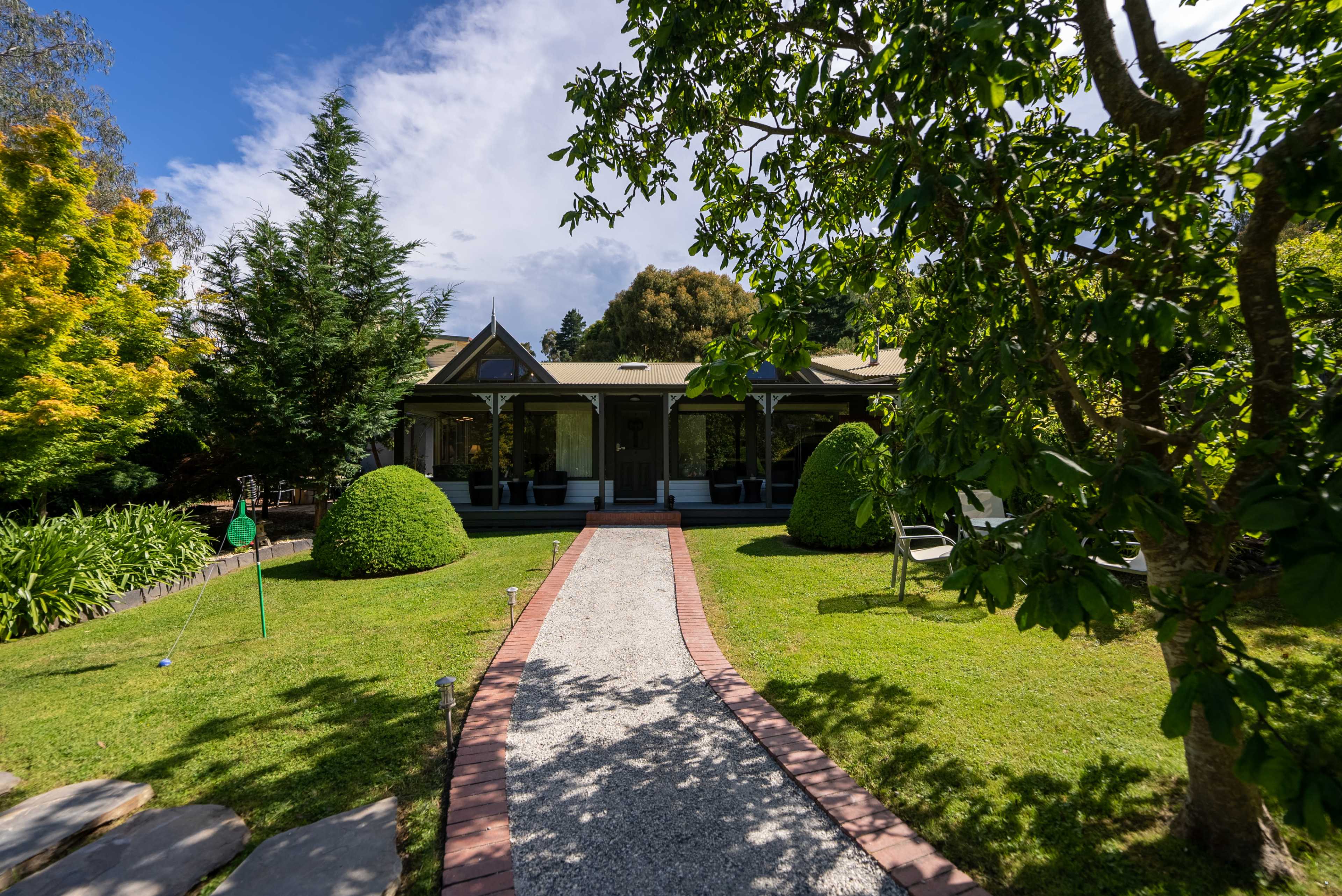 A well-maintained pathway leads to a quaint house surrounded by neatly trimmed hedges and a lush green lawn.