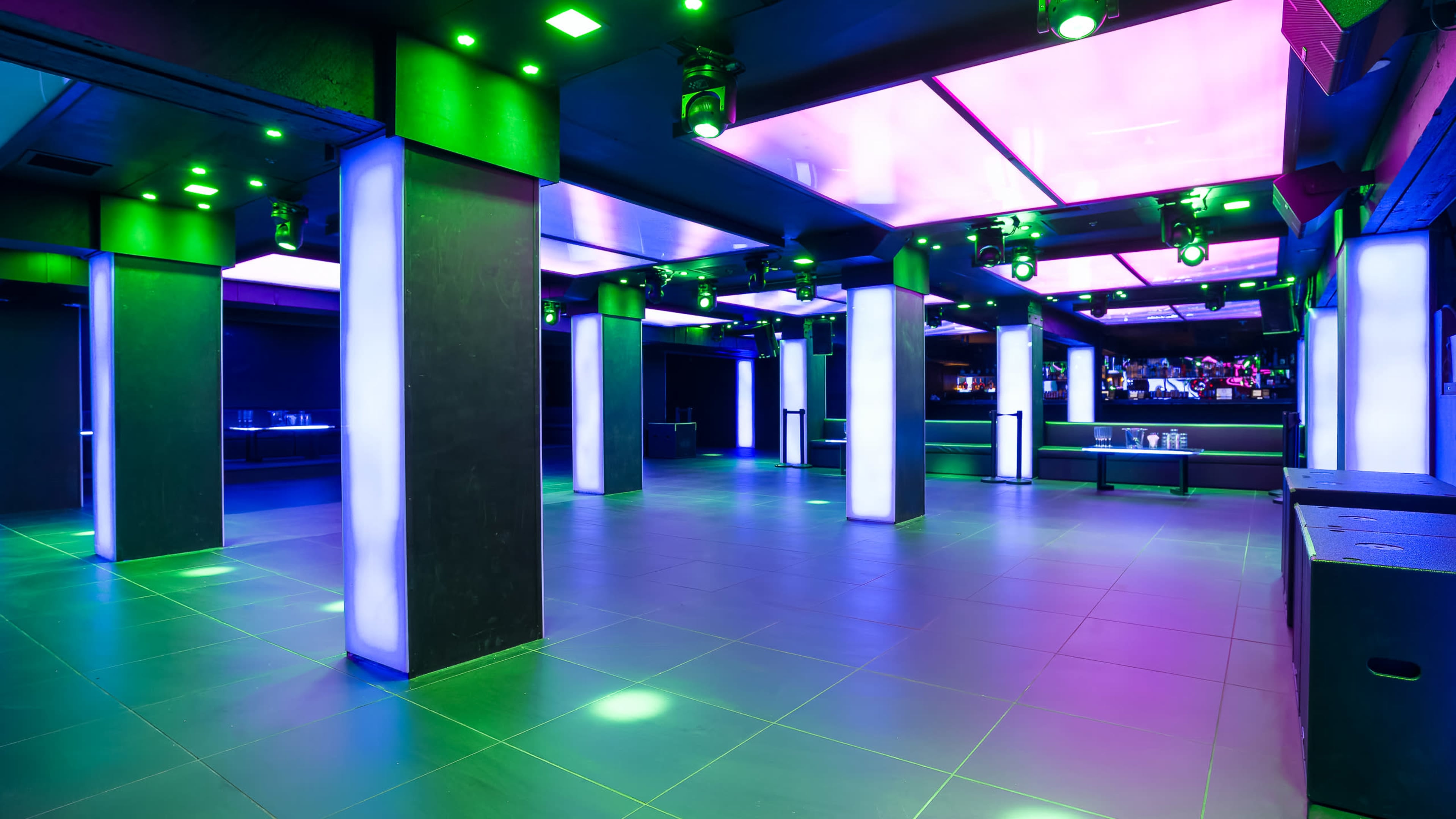 A spacious nightclub interior with illuminated columns and colored lighting fixtures on the ceiling.