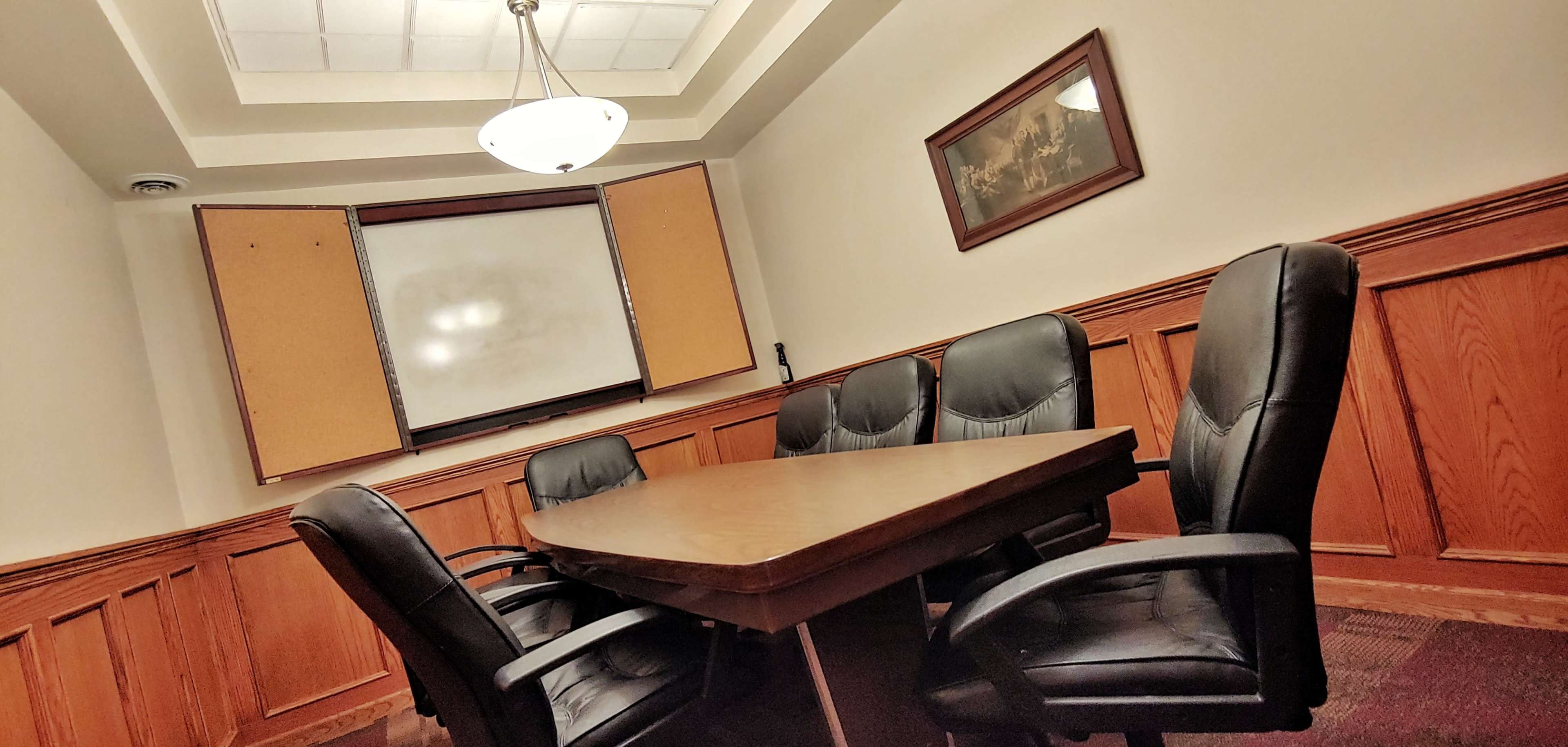 A conference room with a wooden table surrounded by black chairs and a partially closed screen in the background.