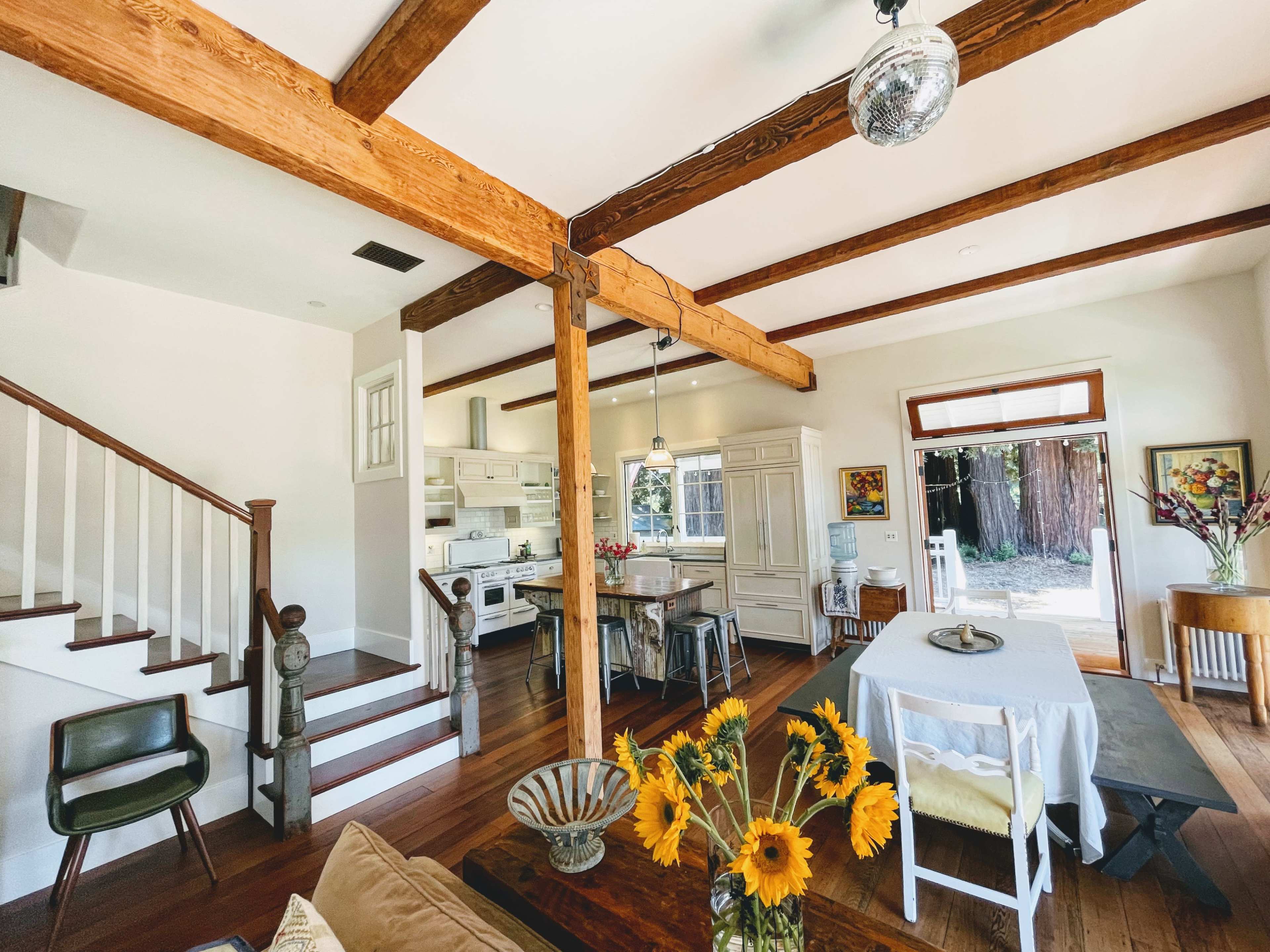 A spacious interior of a house featuring wooden beams, a dining area with a table, and a staircase leading to an upper level.