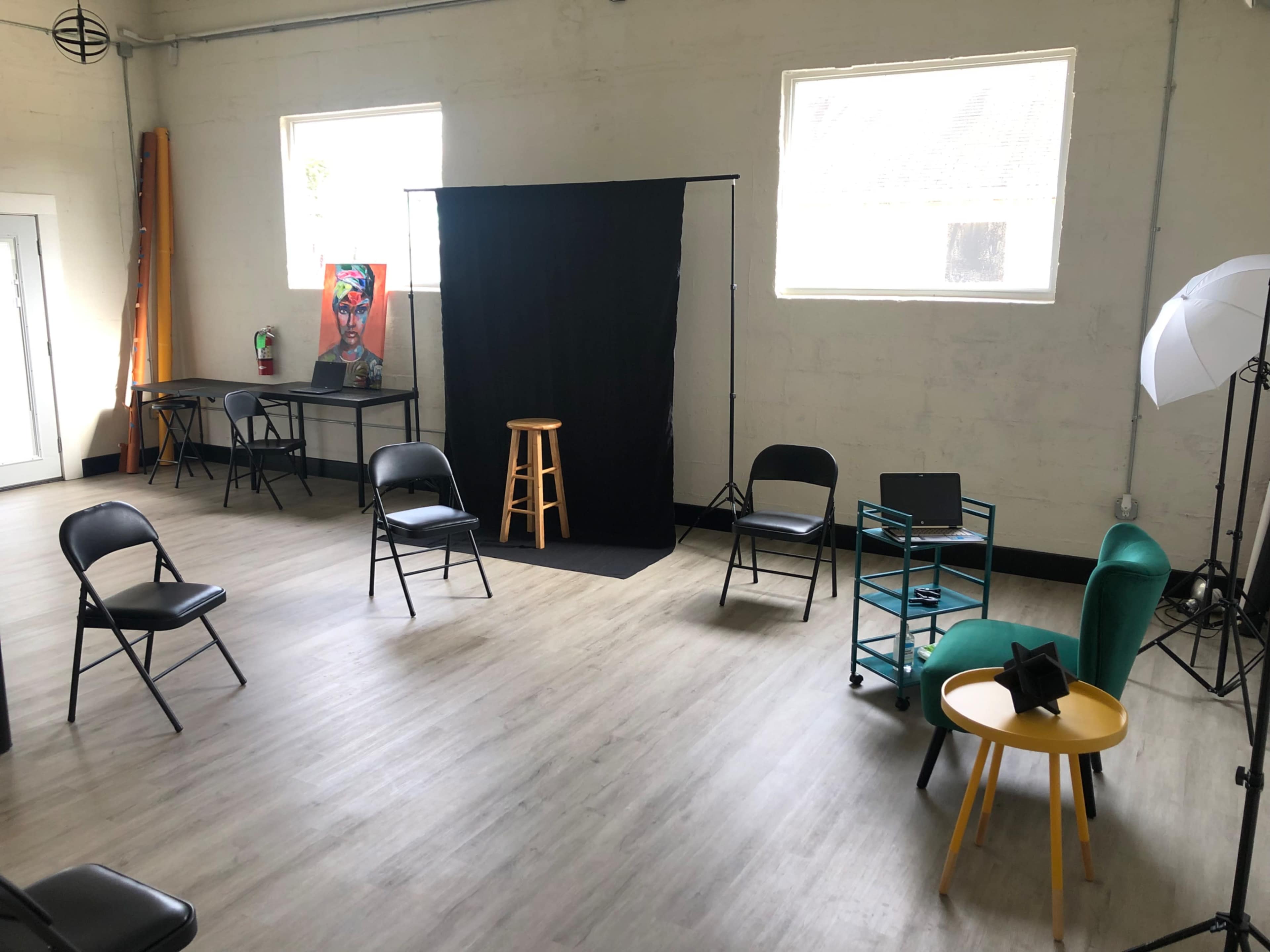 An empty room with a black backdrop, several chairs arranged in a circle, and various furniture items including a stool and tables.