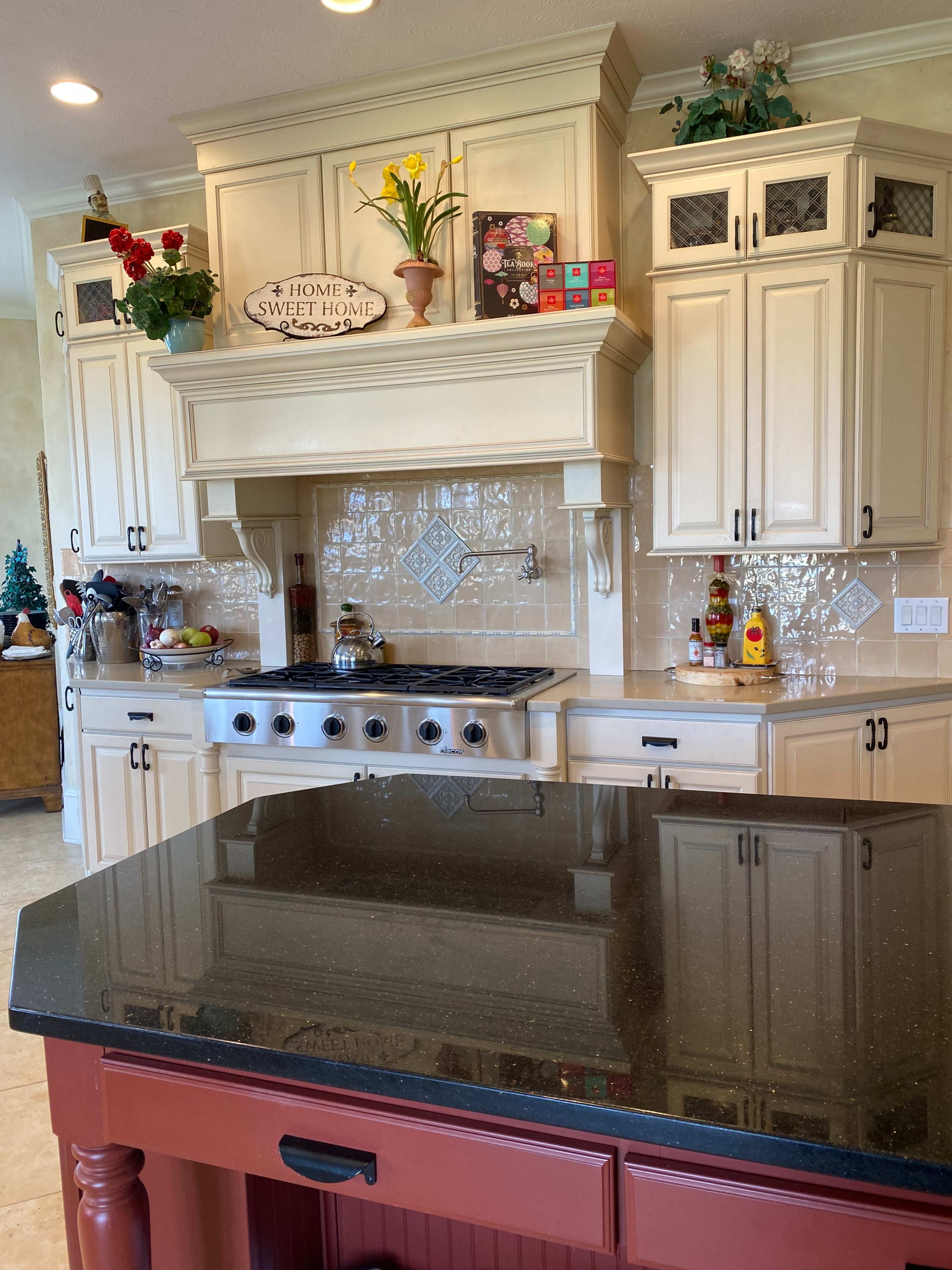 A kitchen with cream-colored cabinets, a black countertop, a stove, and decorative items on the shelves.