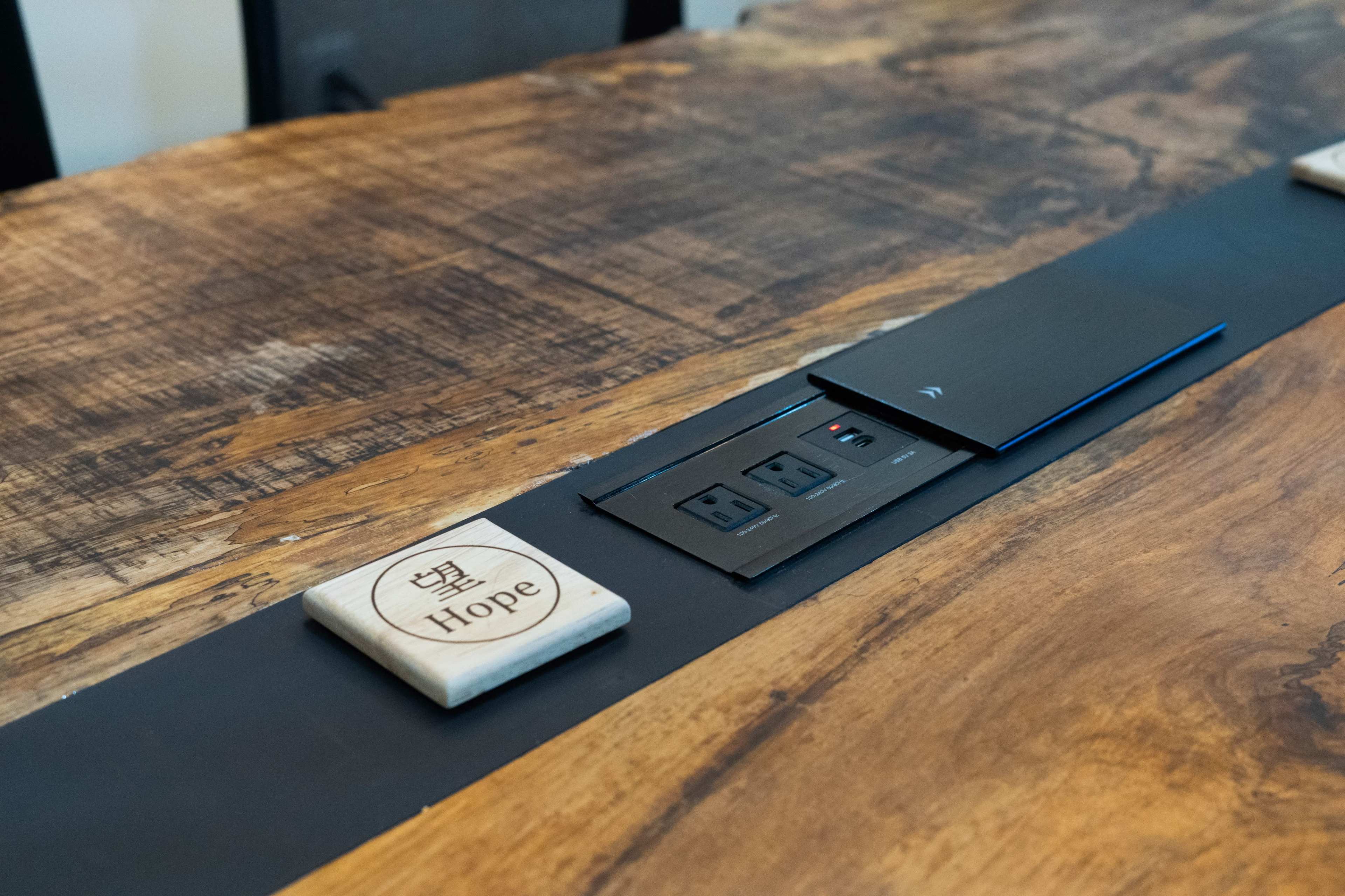 The image shows a wooden table with a power outlet and a decorative tile labeled "Hope" integrated into a black strip running along the center.