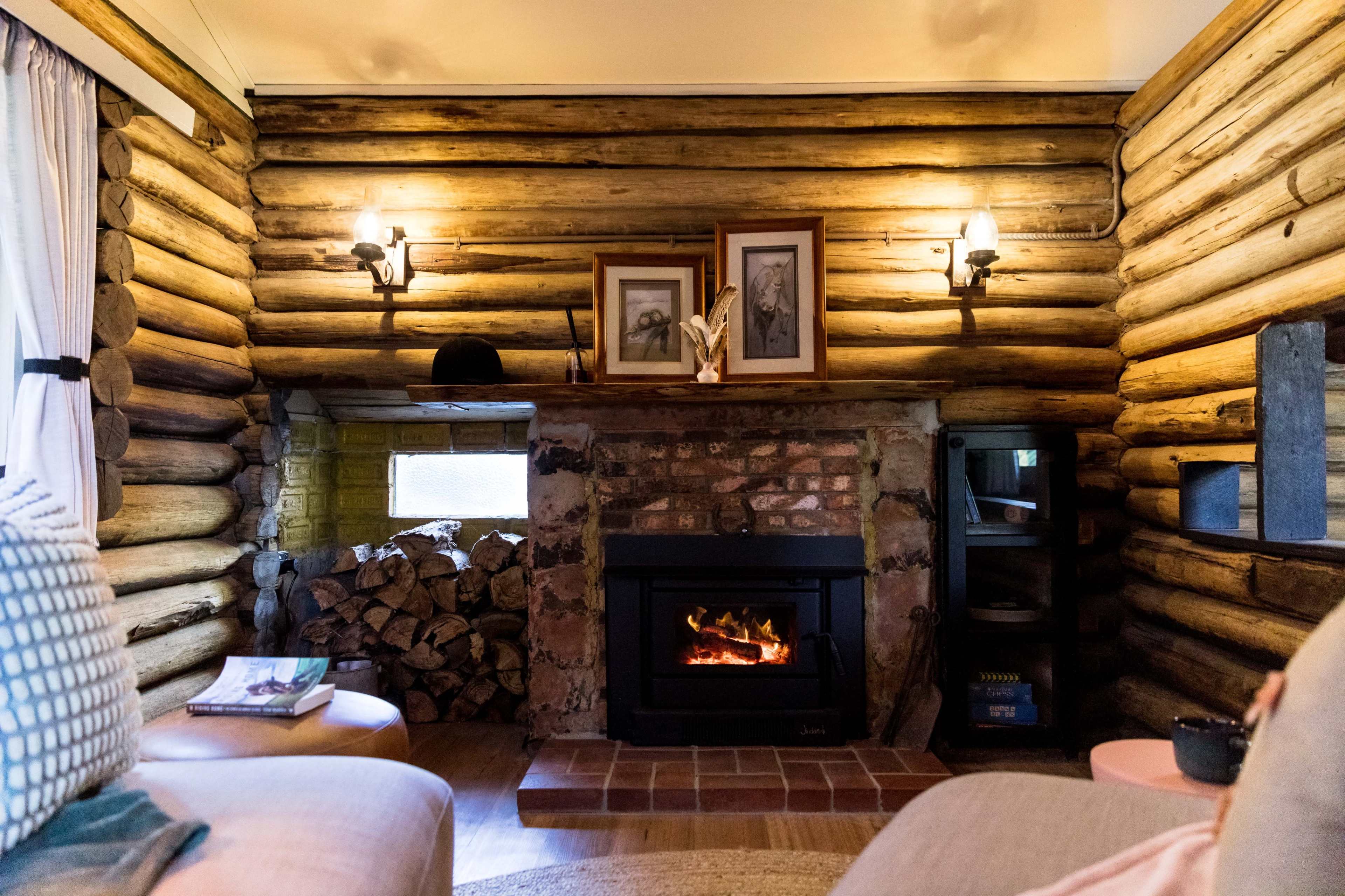 A cozy living room with log cabin walls, a fireplace with a fire burning, and framed pictures on the wall above it.