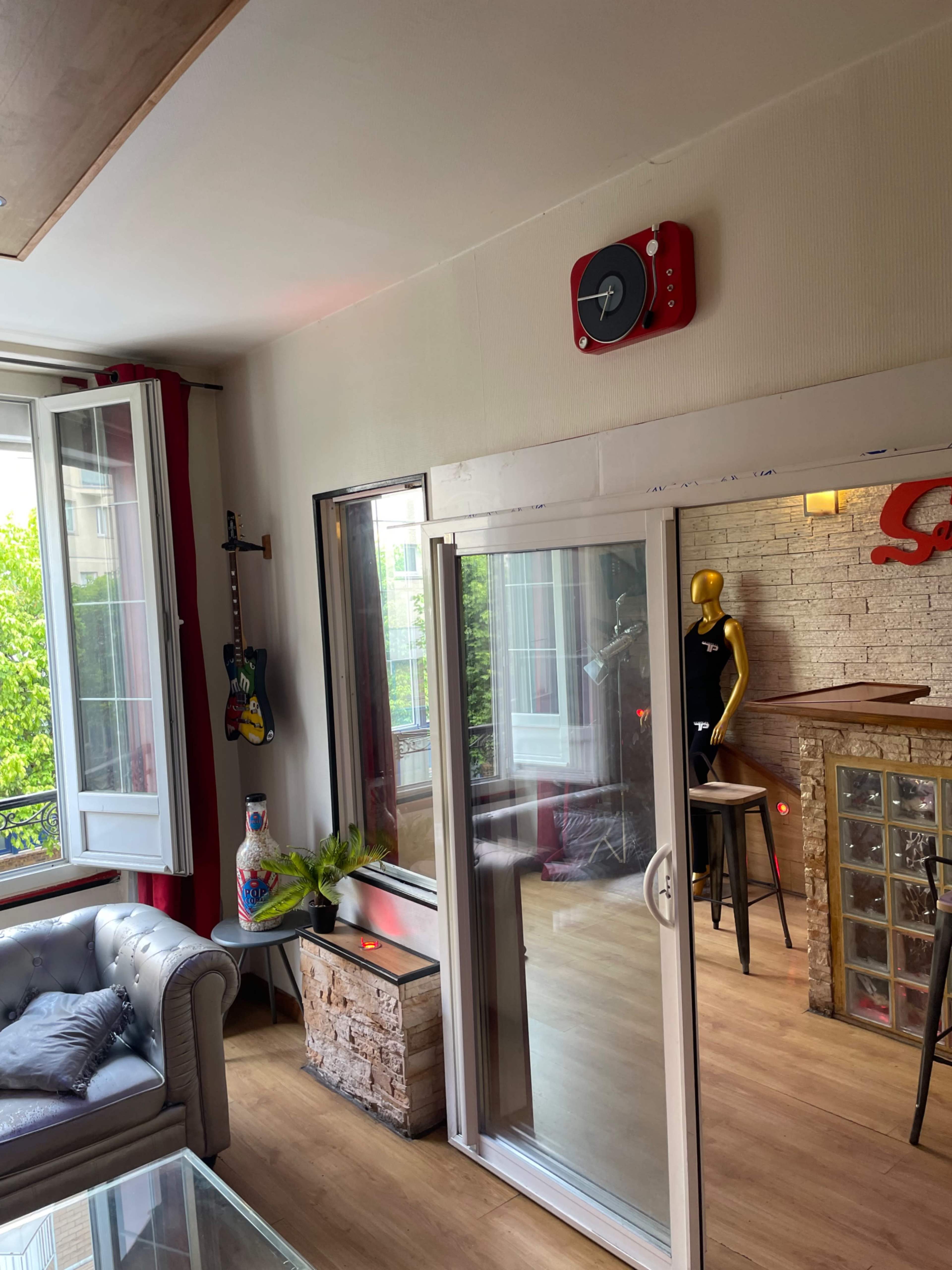 A living room with a large window, a guitar on the wall, a glass door leading to an outside area, and a red speaker mounted on the wall.