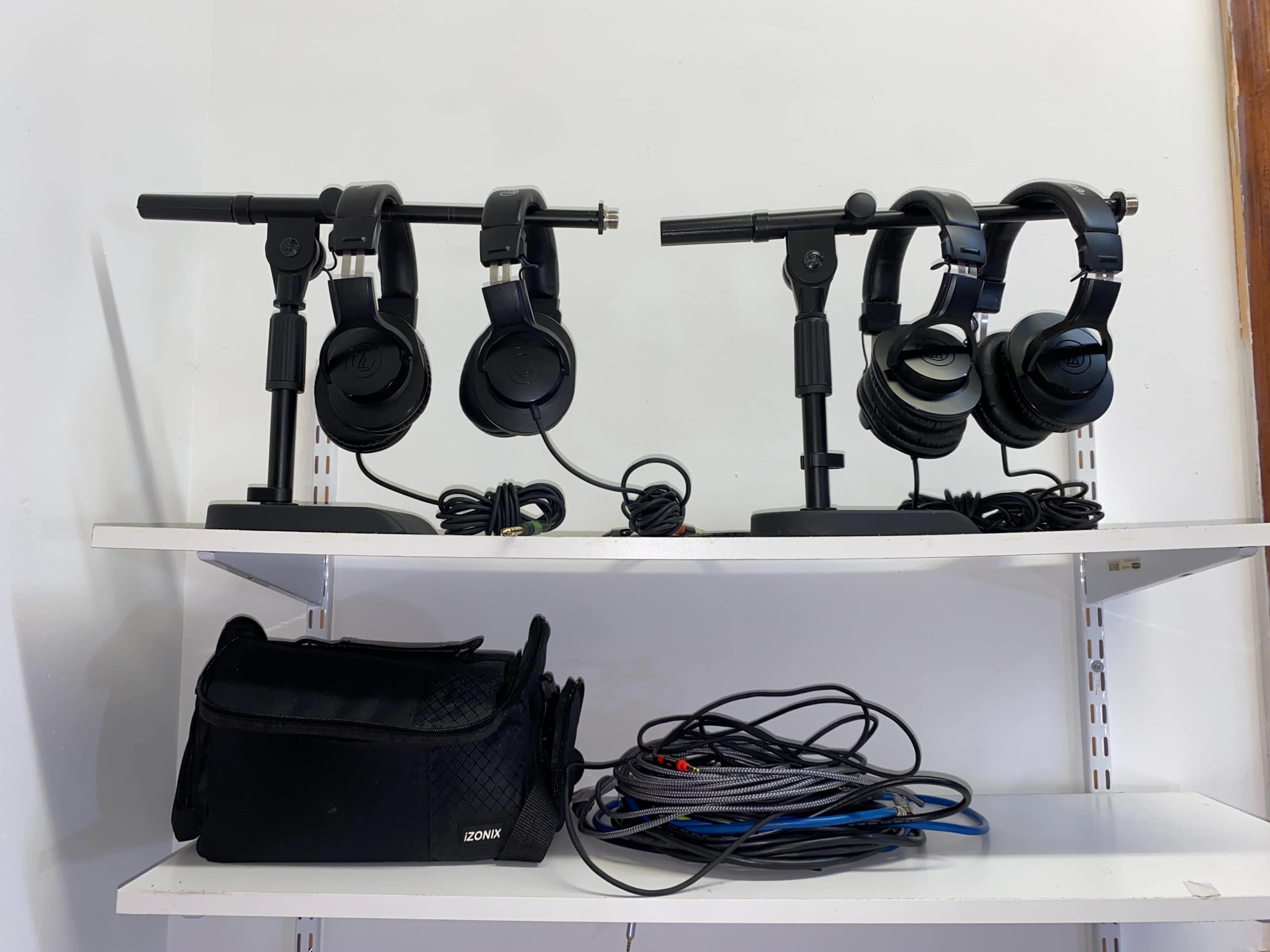 The image shows a shelf with two headphone stands holding black headphones, alongside a bag and tangled cables.