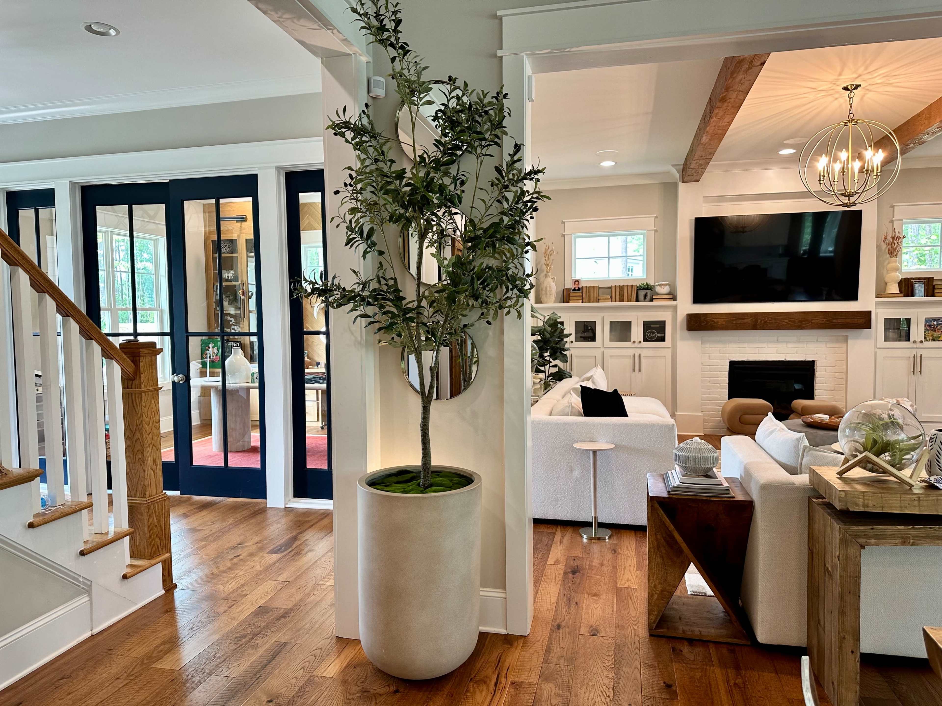 A modern interior space featuring a staircase, a large potted plant, and a living area with a television and comfortable seating.