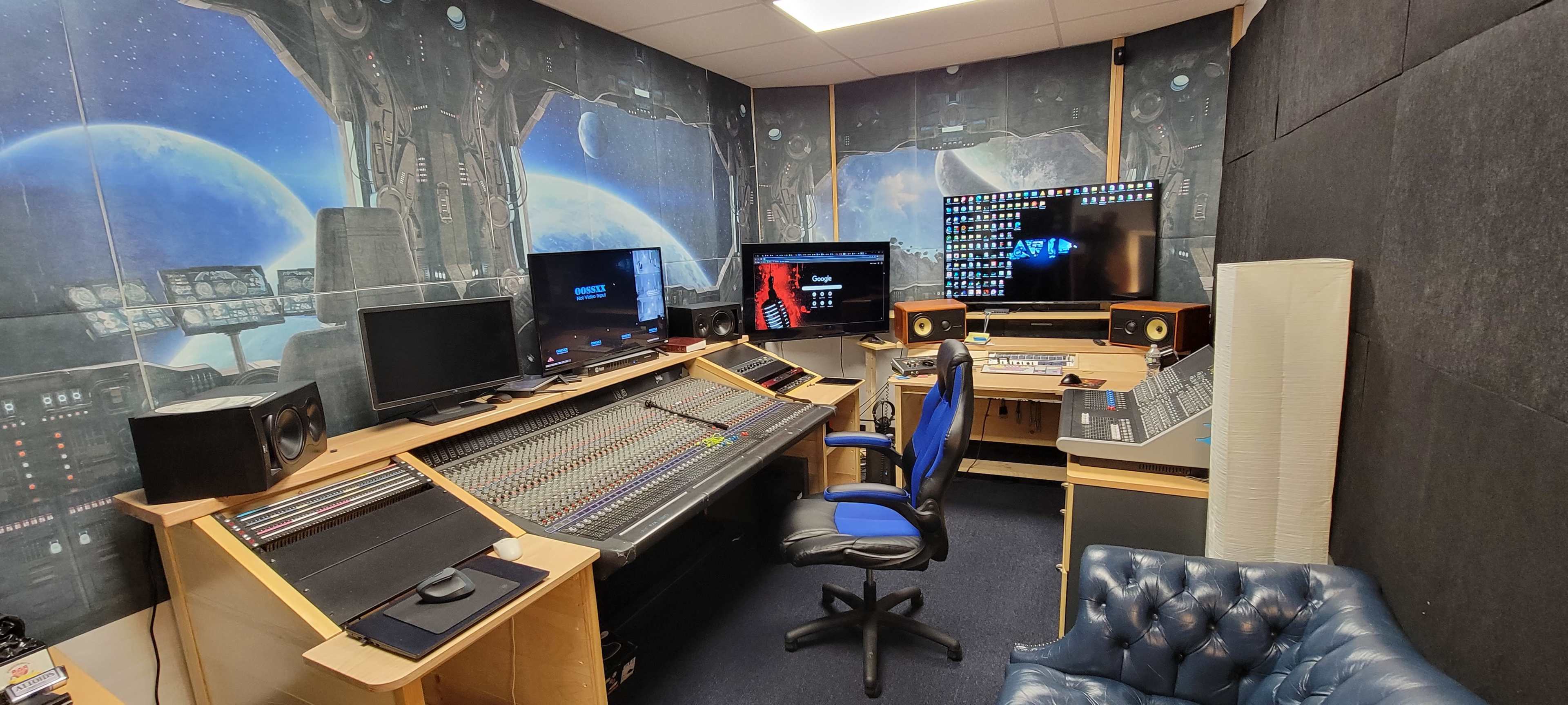 A recording studio featuring a large mixing console, computer monitors, and a blue office chair, all set against a space-themed backdrop.