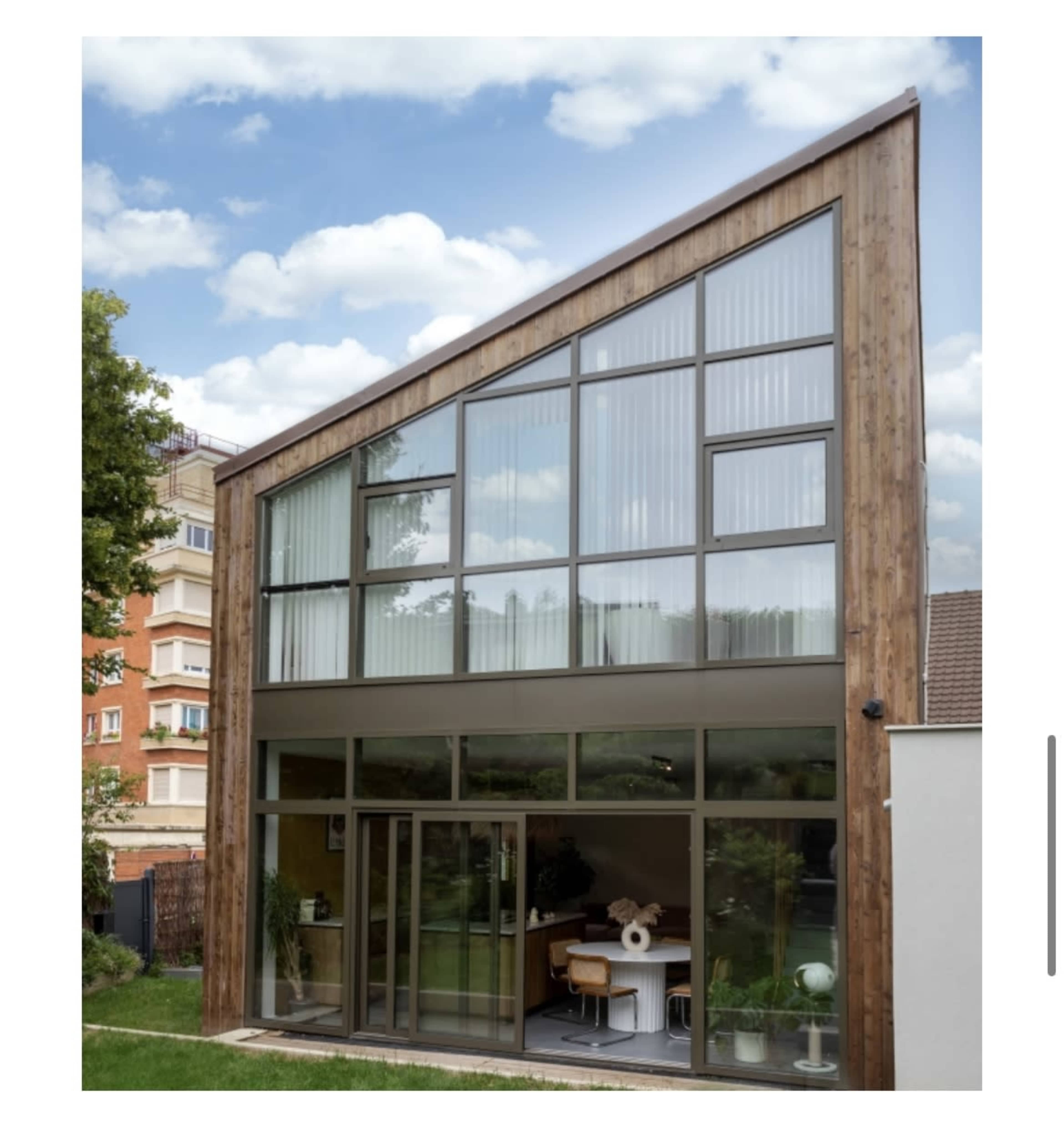A modern home featuring a large glass facade and a wooden exterior, set against a cloudy sky.