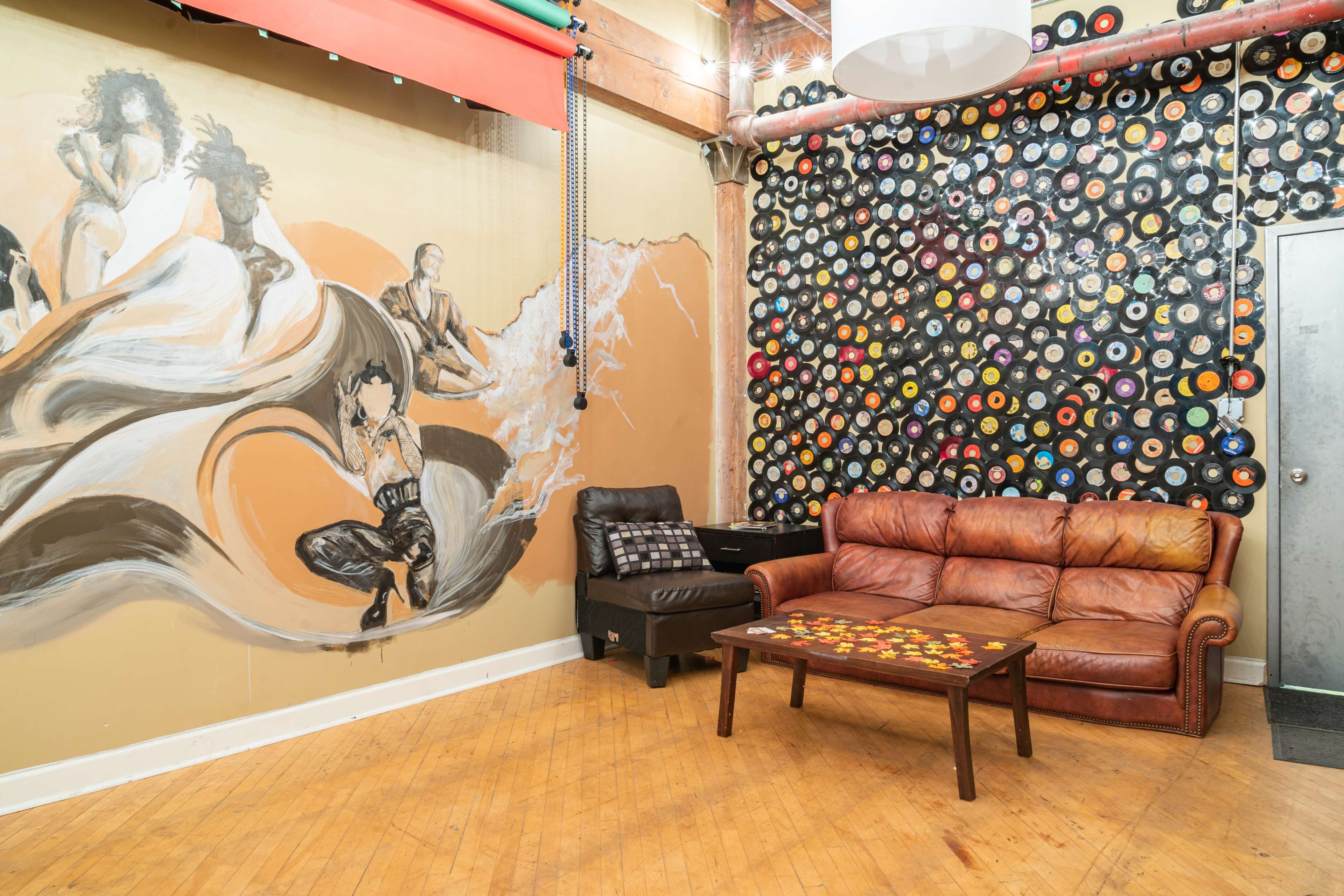 A cozy lounge area featuring a leather couch, a coffee table decorated with colorful items, and a wall adorned with a mural and a collection of vinyl records.