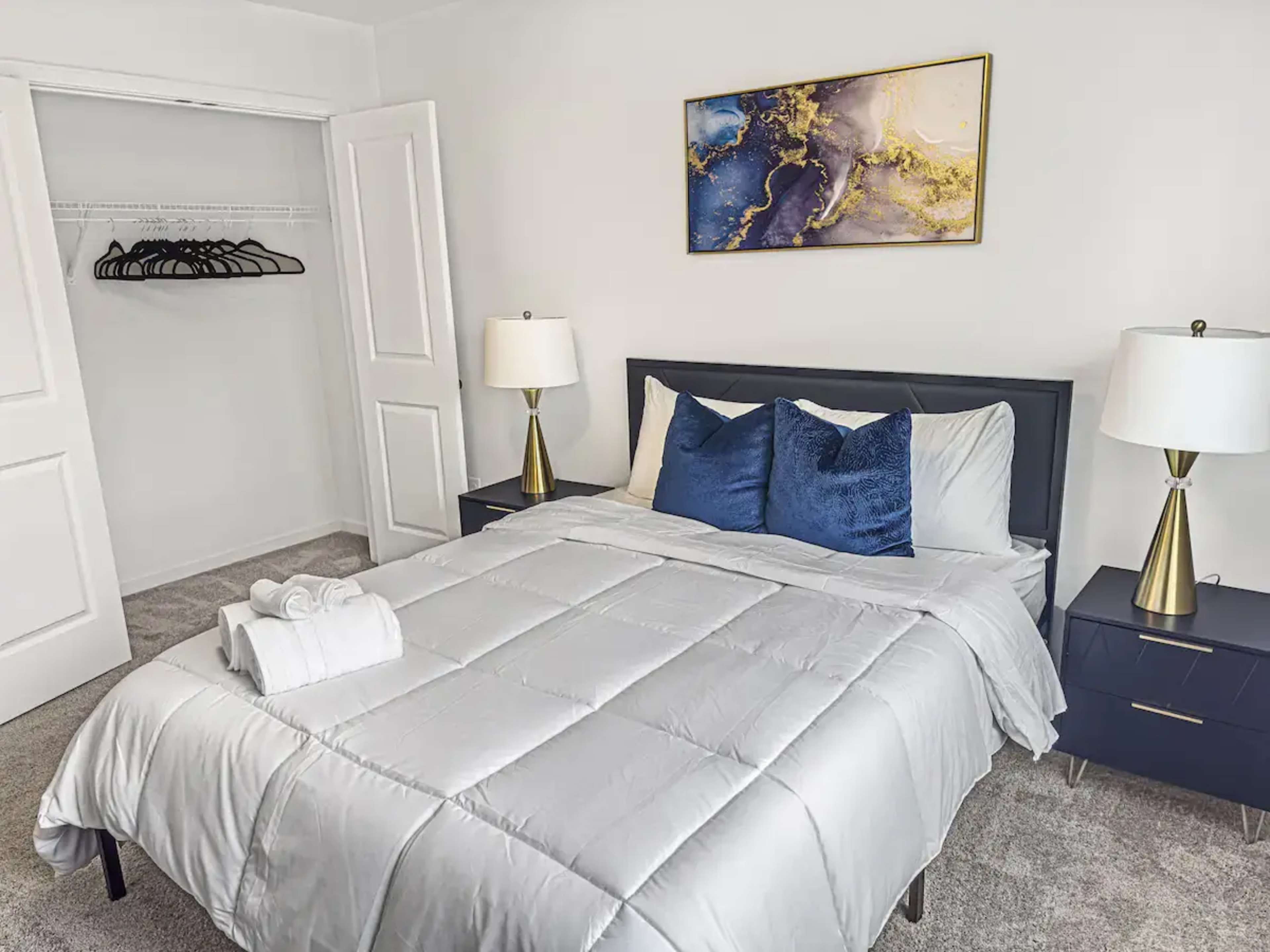 The image shows a neatly arranged bedroom with a bed, two bedside lamps, and a closet in the background.