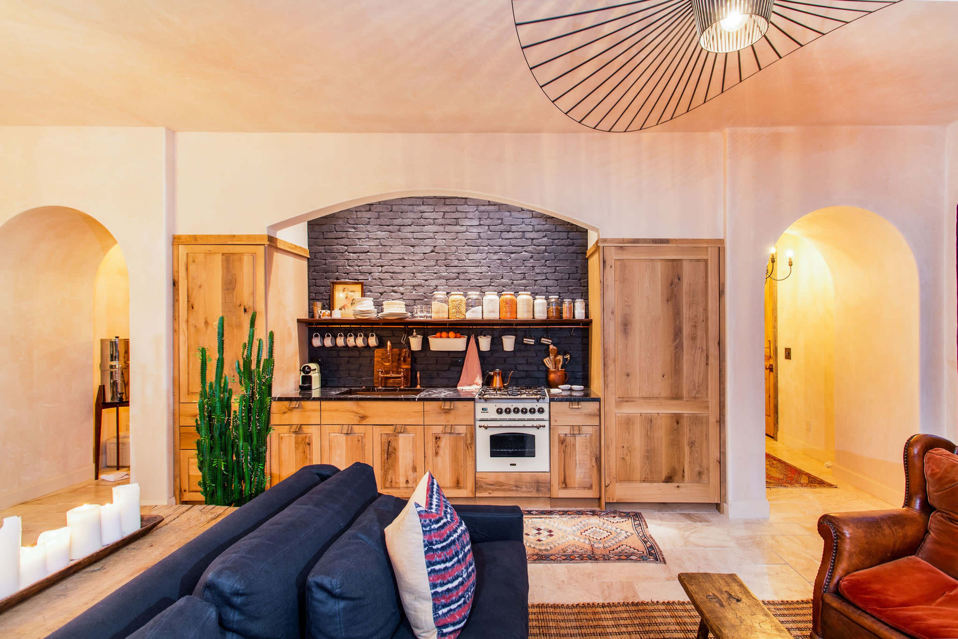 A modern kitchen features wooden cabinetry, a stone backsplash, and a gas stove, with a cozy living area visible in the foreground.