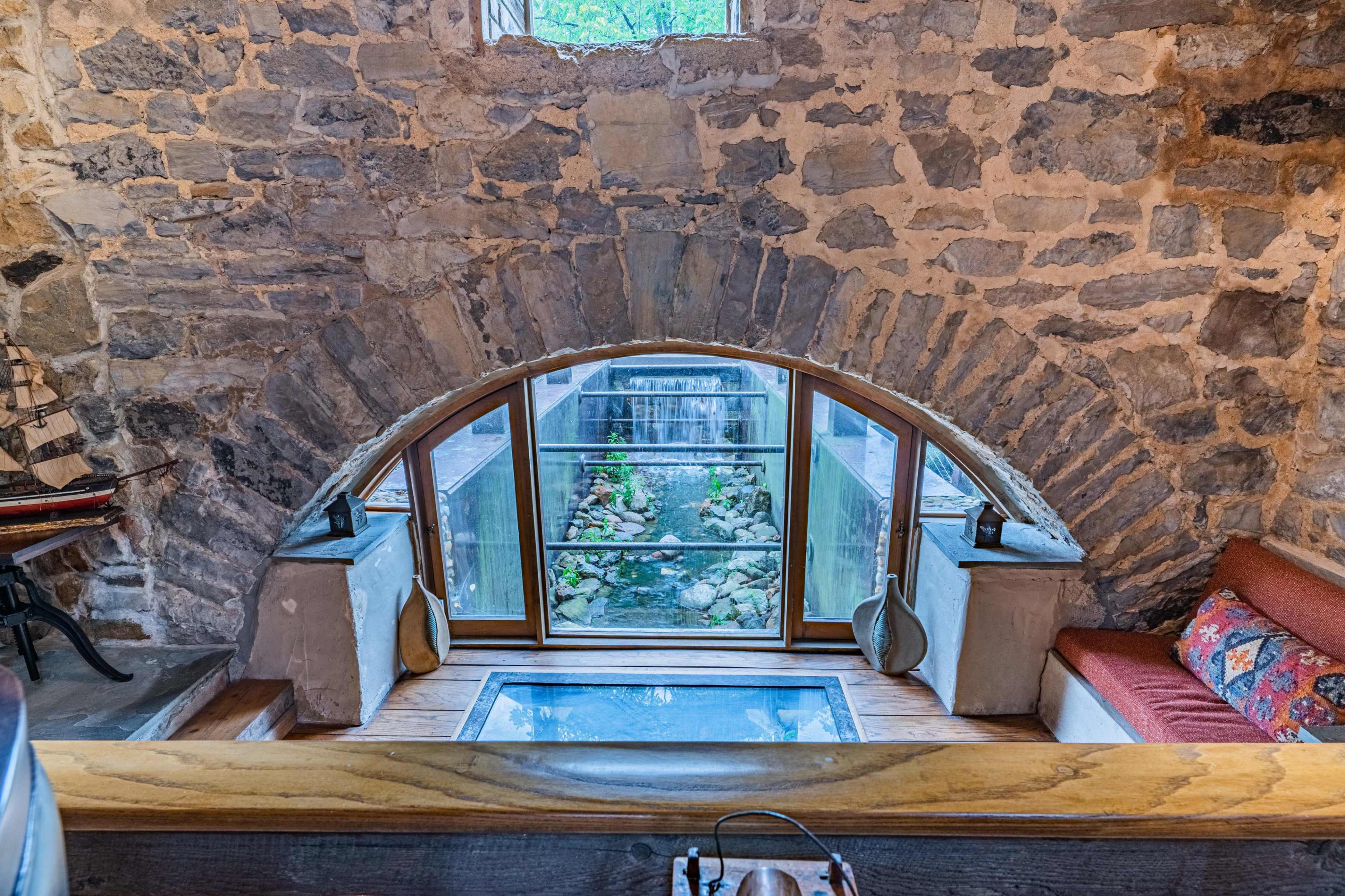 A cozy interior featuring an arched stone window framing a view of a small water feature surrounded by greenery.