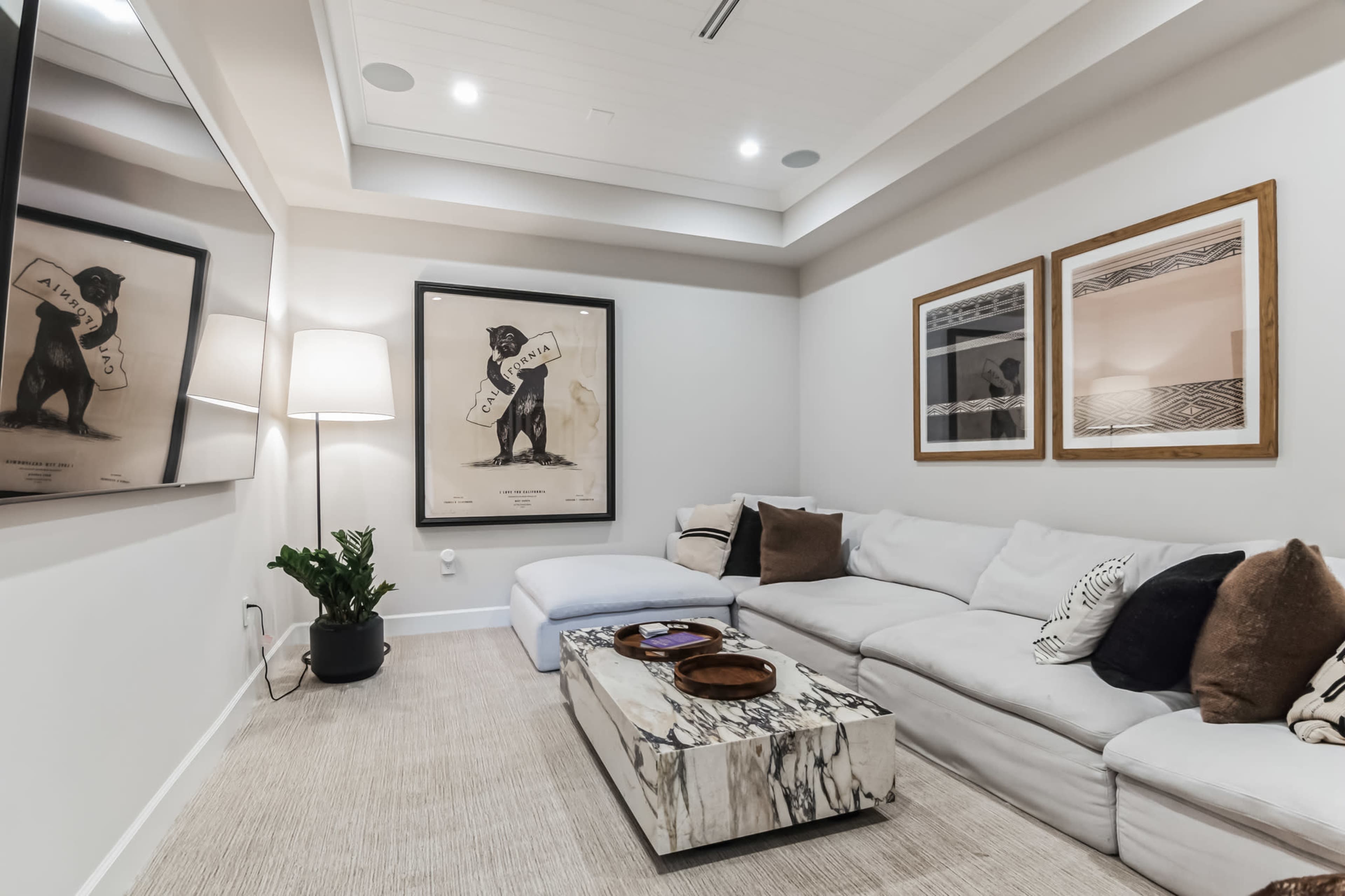 A modern living room features a white sectional sofa, a marble coffee table, framed artwork on the walls, and a standing lamp beside it.