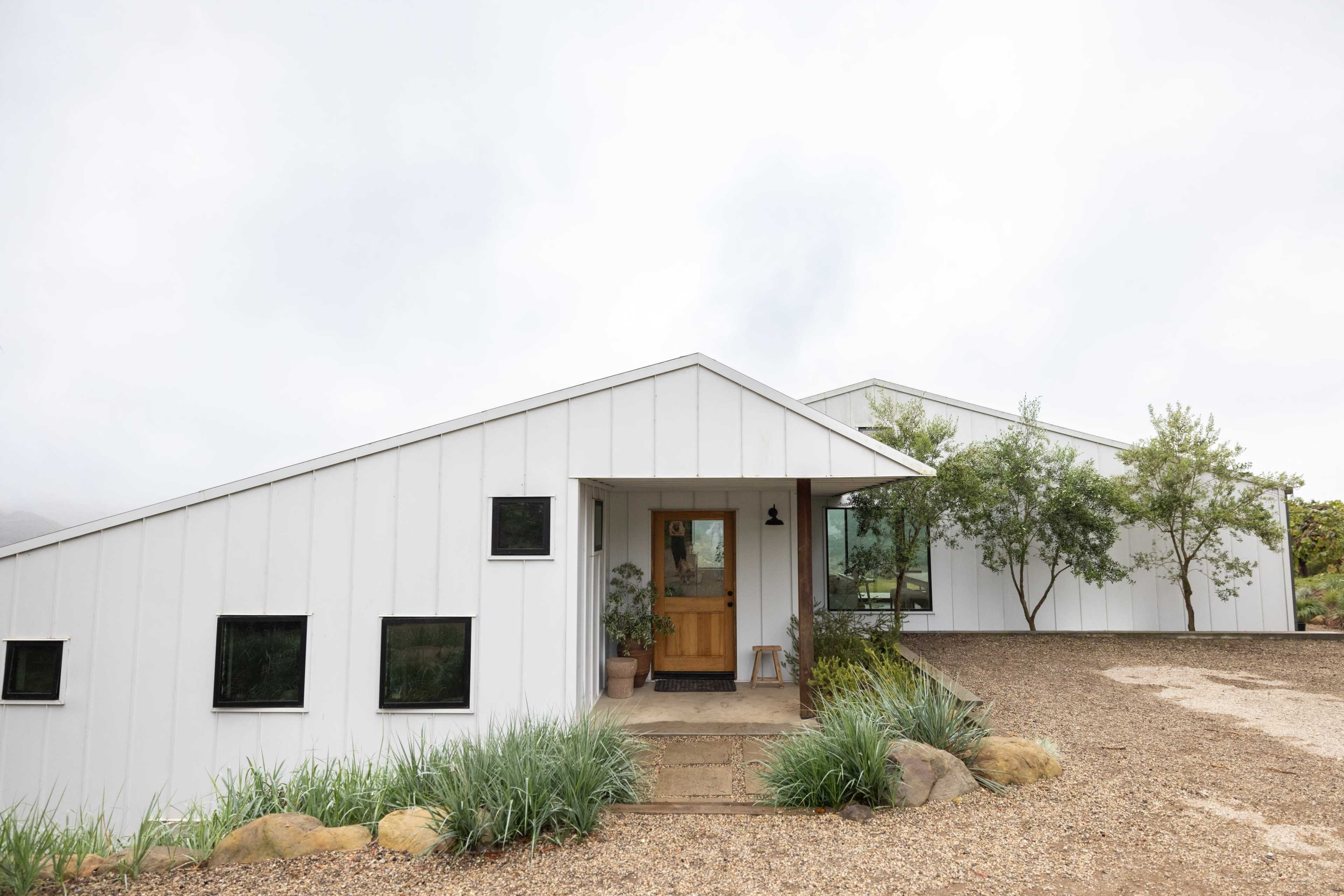 A modern white house with a sloped roof is set in a gravel landscape featuring small plants and shrubs.