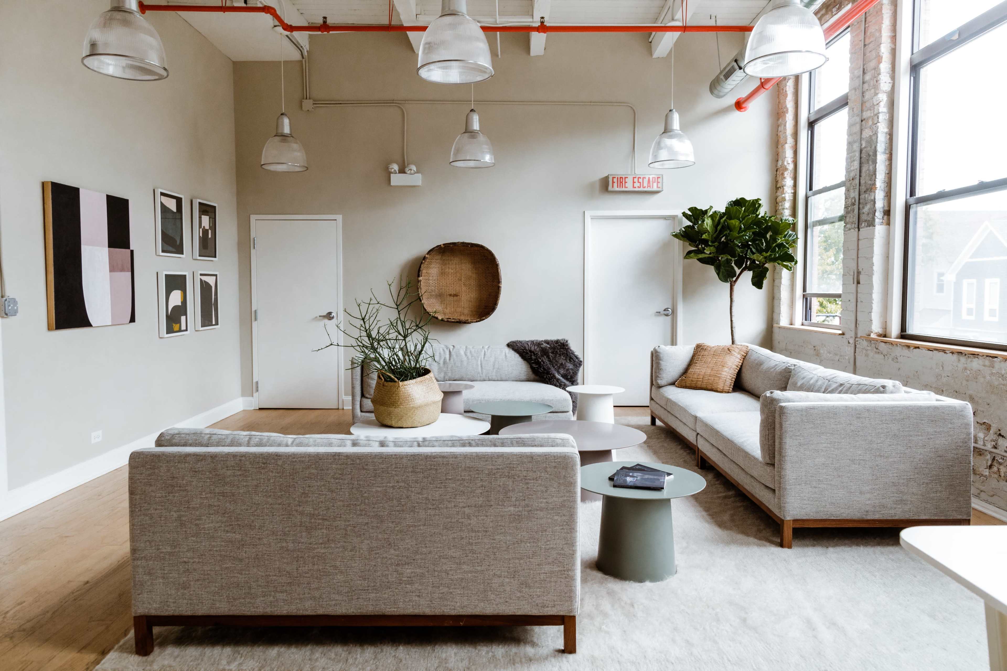 A modern living room features two gray sofas, a round coffee table, and art on the walls, with large windows allowing natural light.