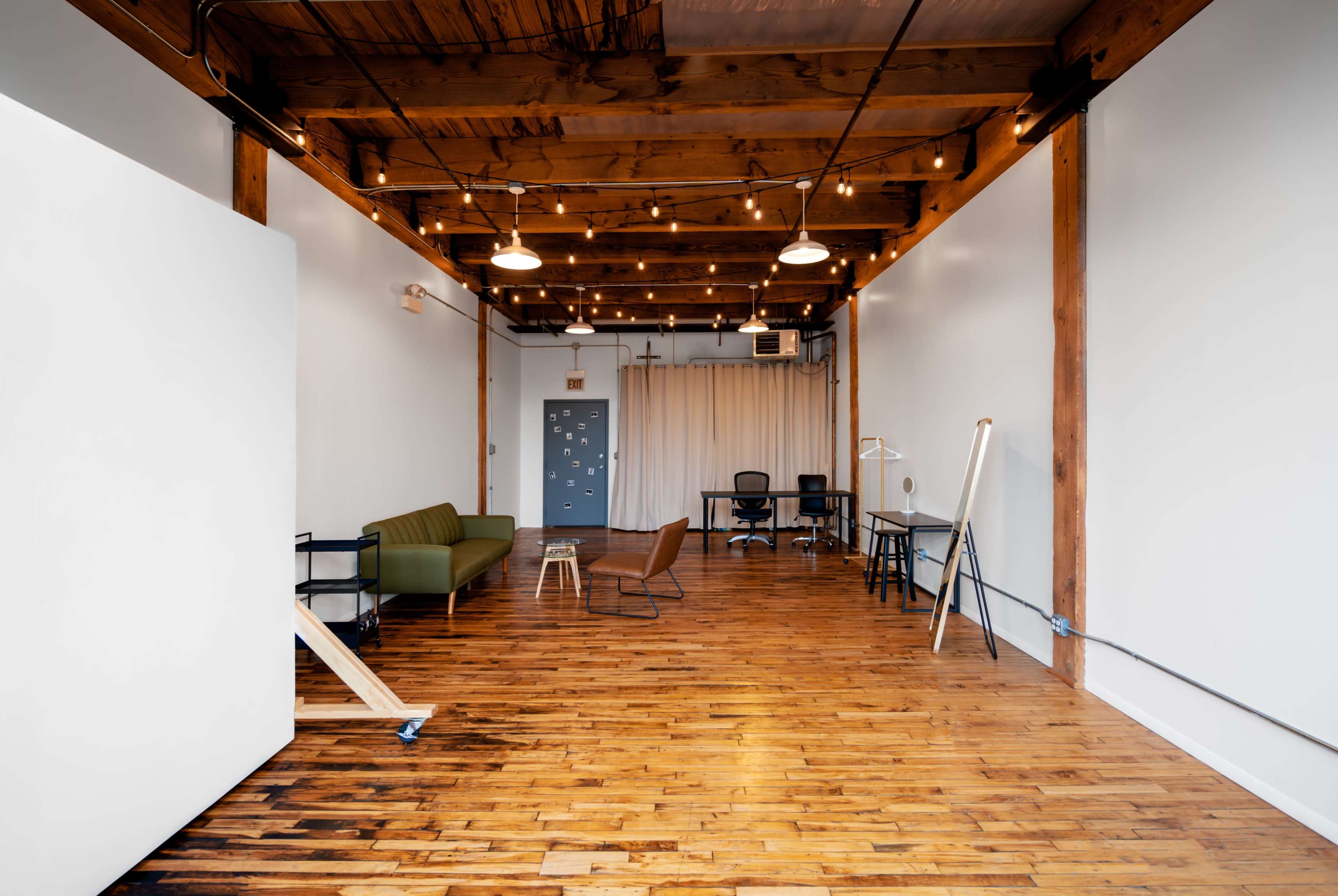 A well-lit, spacious office interior featuring wooden floors, exposed beams, and a mix of seating and workspaces.