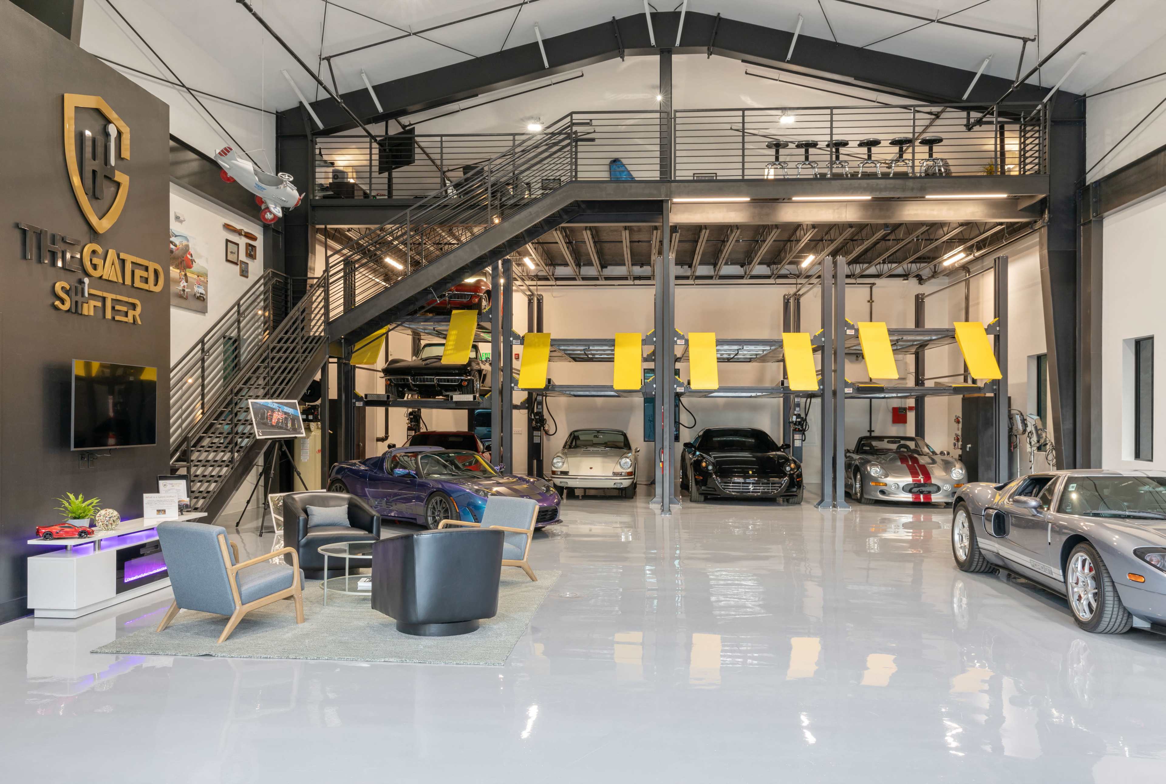 The image shows a modern garage with several luxury cars parked on the ground floor and a mezzanine level above.