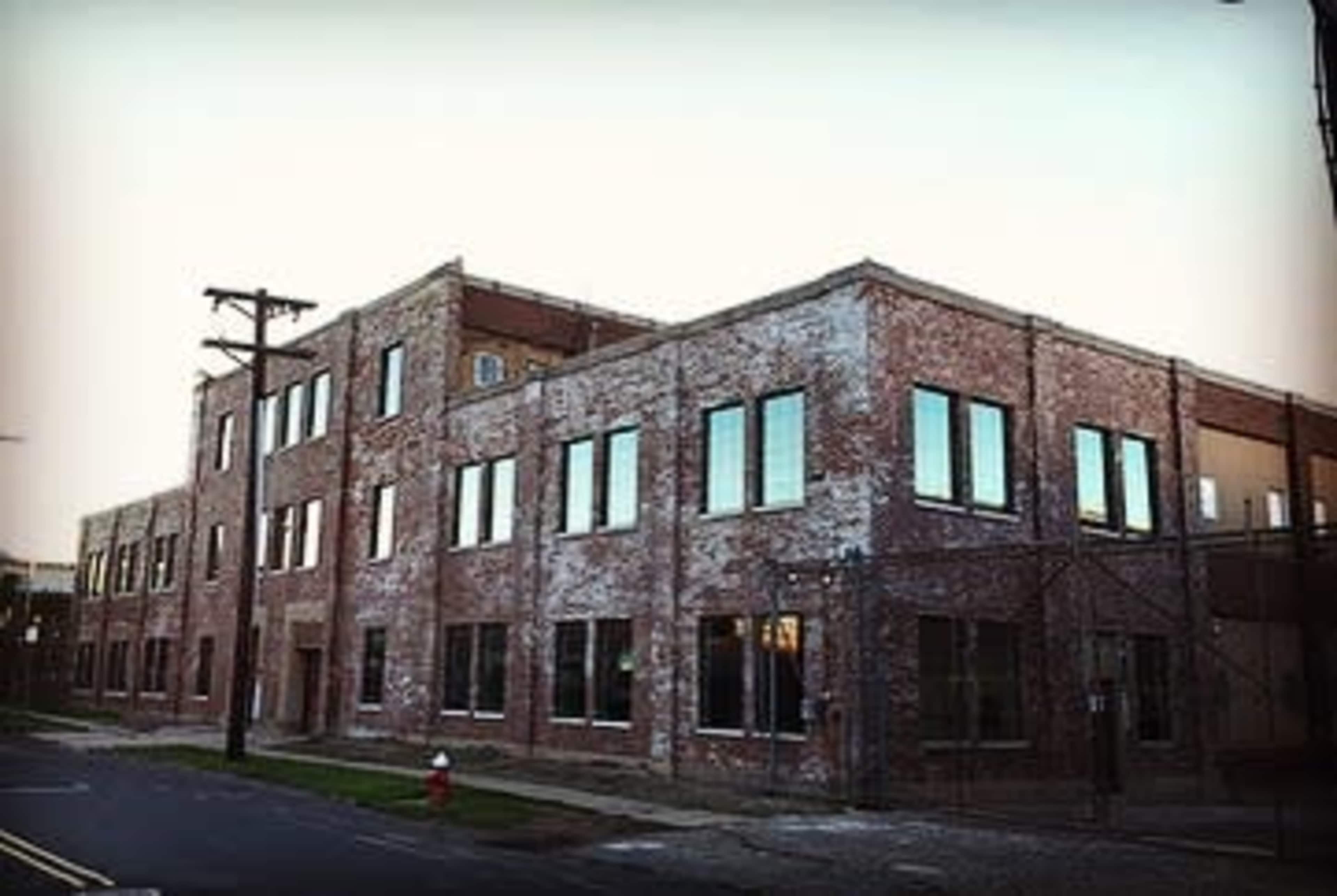 The image shows a large, brick building with multiple windows, located on a street with a fire hydrant nearby.