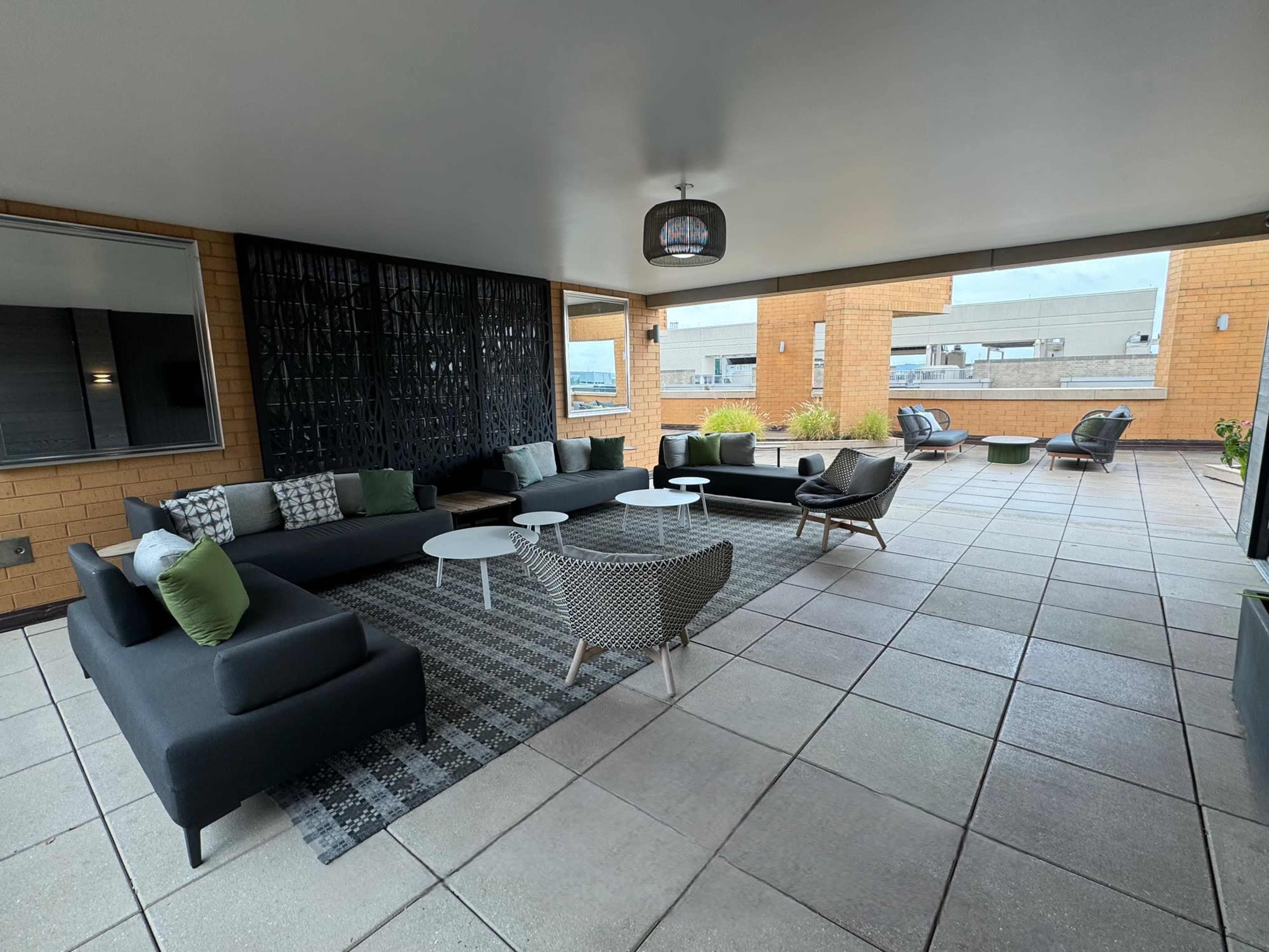 A spacious rooftop lounge area with modern seating, tables, and decorative plants on a tiled surface.