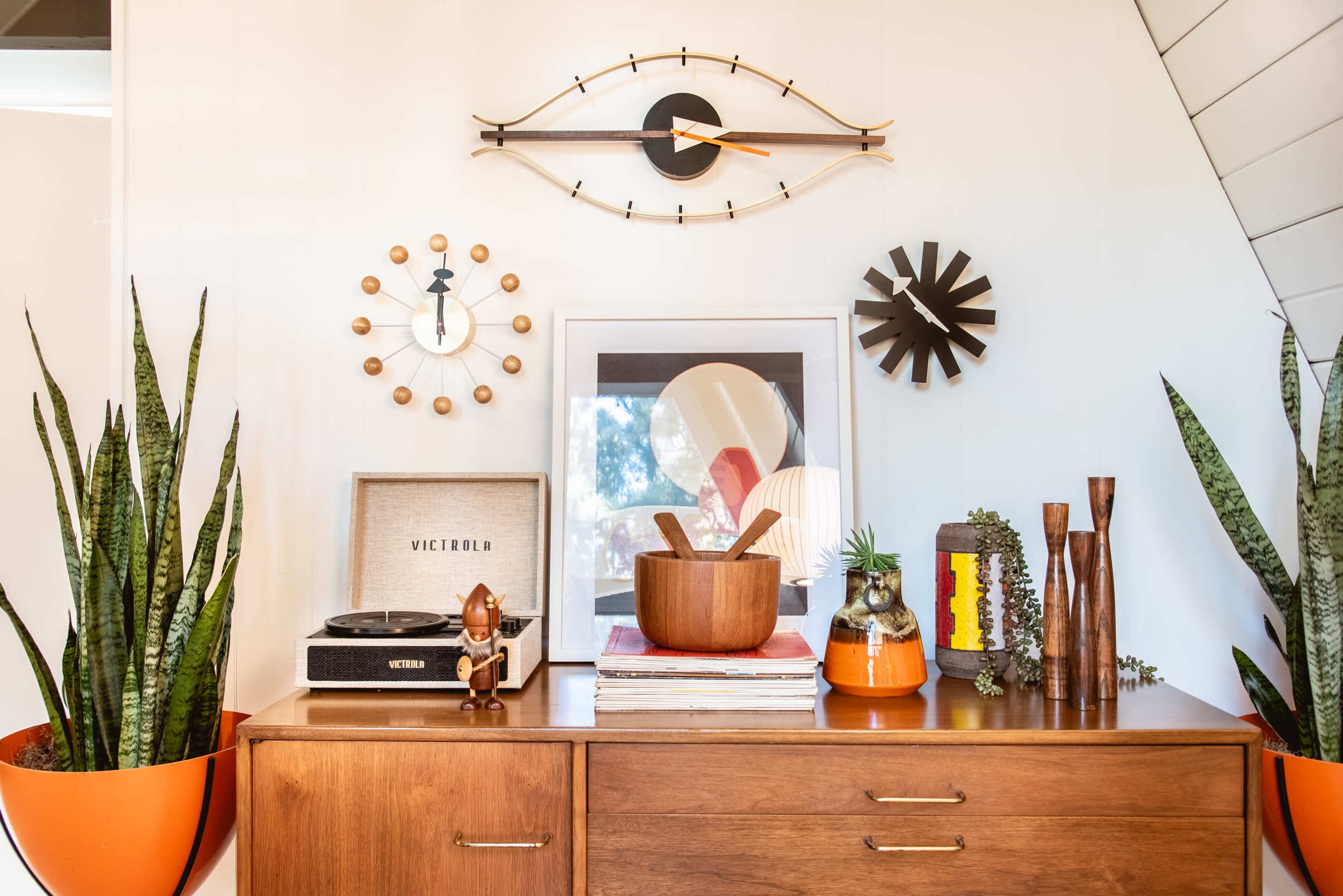 A wooden sideboard displays a vintage record player, decorative items, and plants against a white wall.
