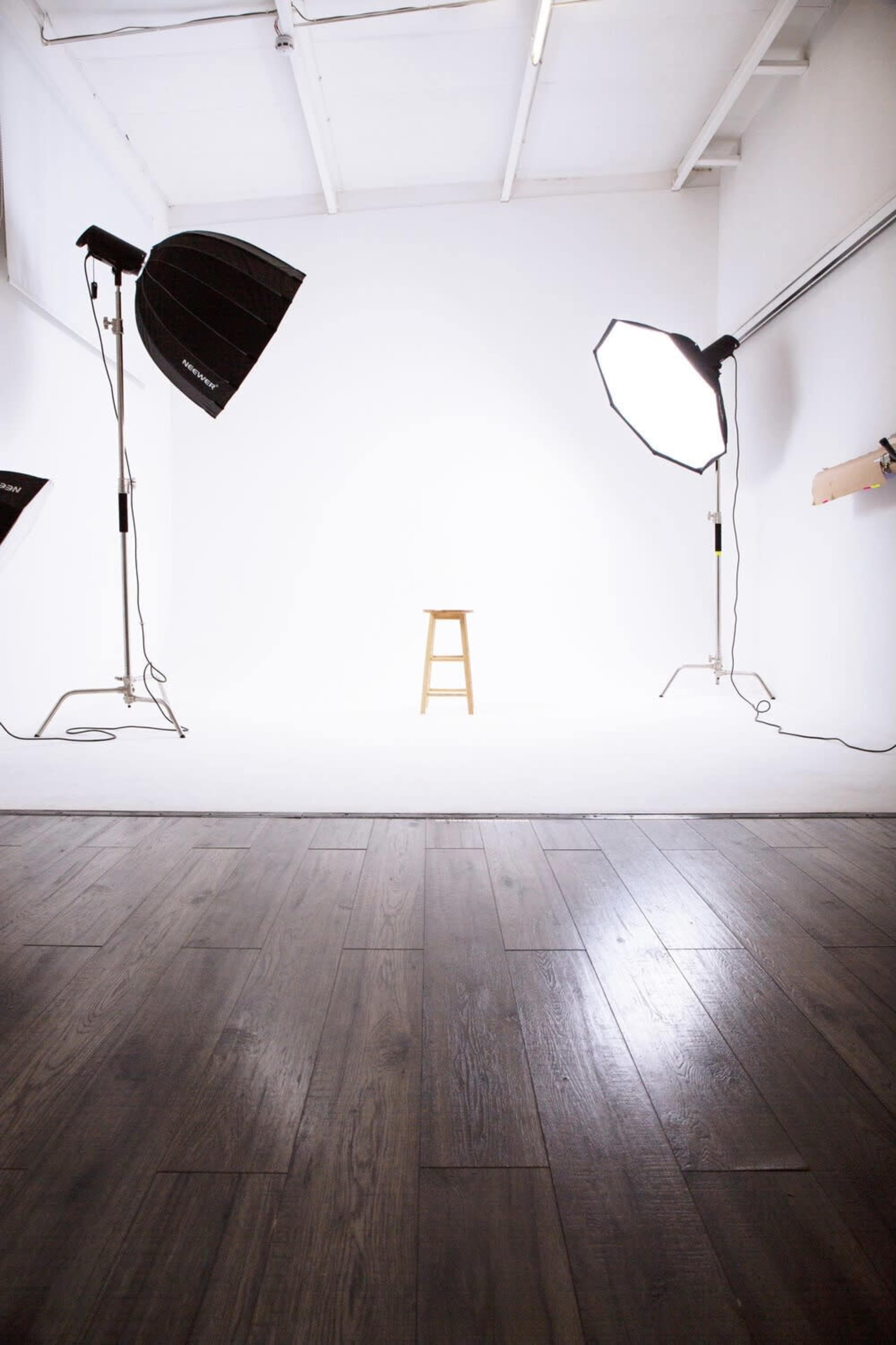 A wooden stool is positioned in the center of a brightly lit photography studio, surrounded by large light sources.
