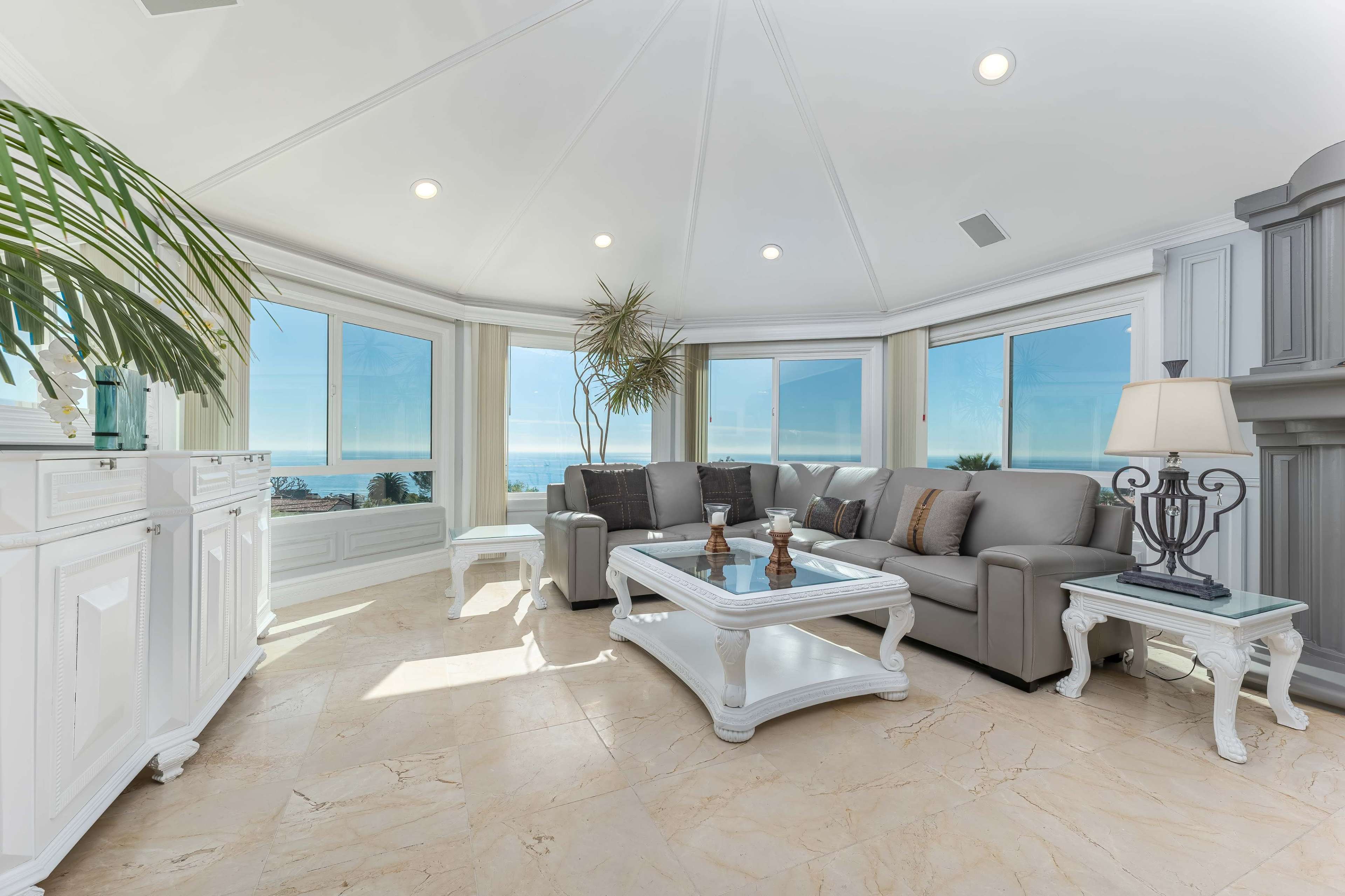 A bright living room features a gray sofa, a coffee table, and large windows with ocean views.