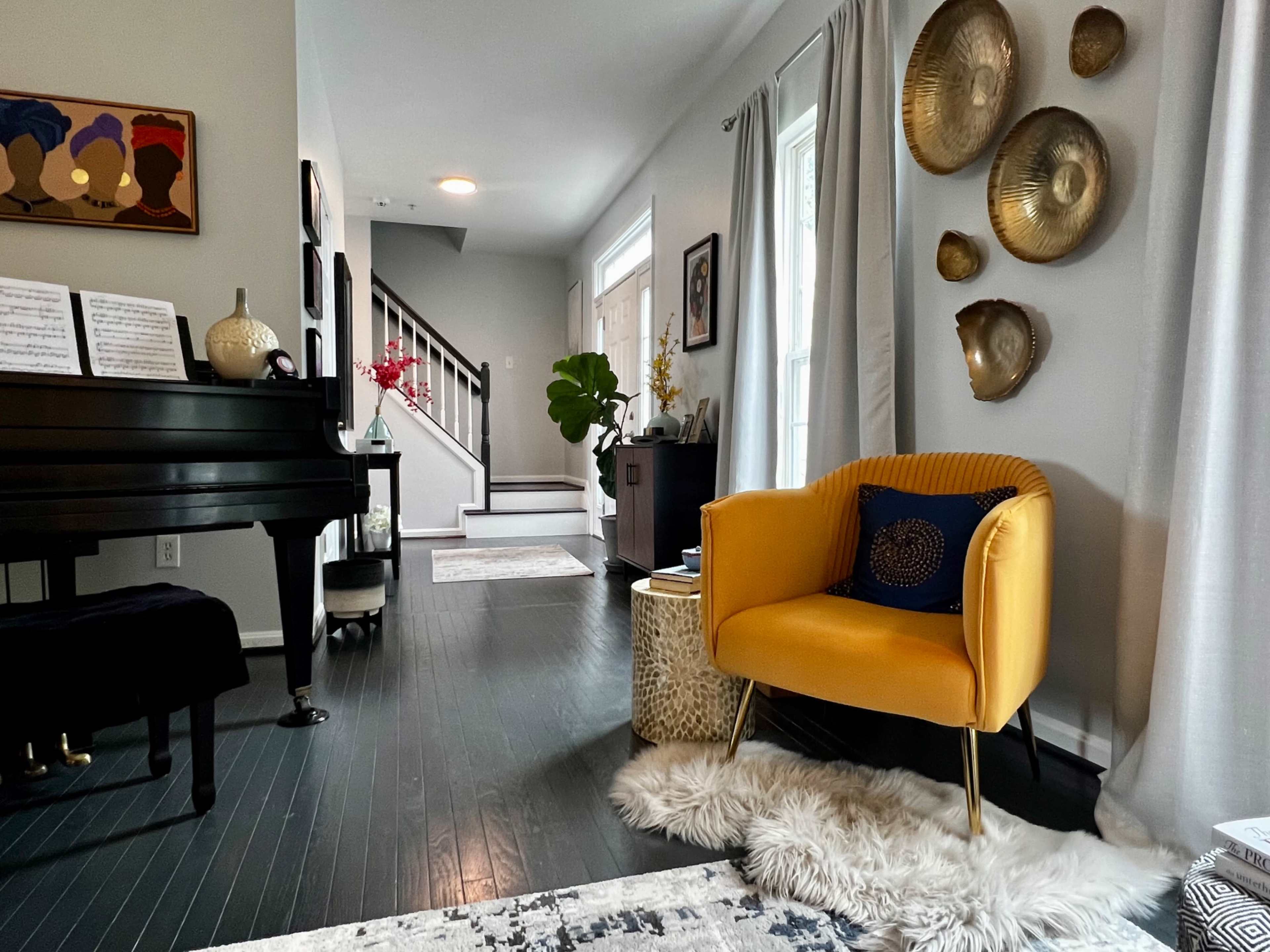 A modern living room features a black piano, a yellow armchair, and decorative wall plates, with a staircase in the background.