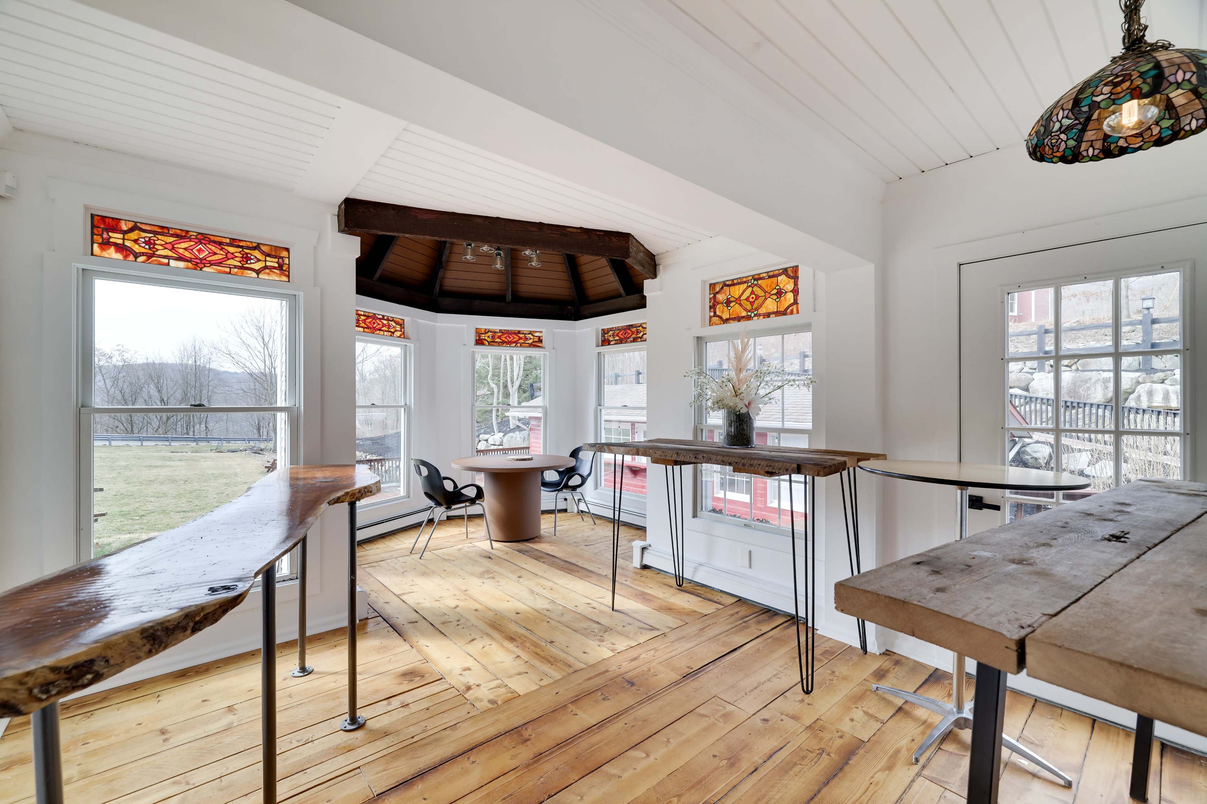 A bright, airy room with large windows, wooden floors, and a central round table surrounded by modern chairs.