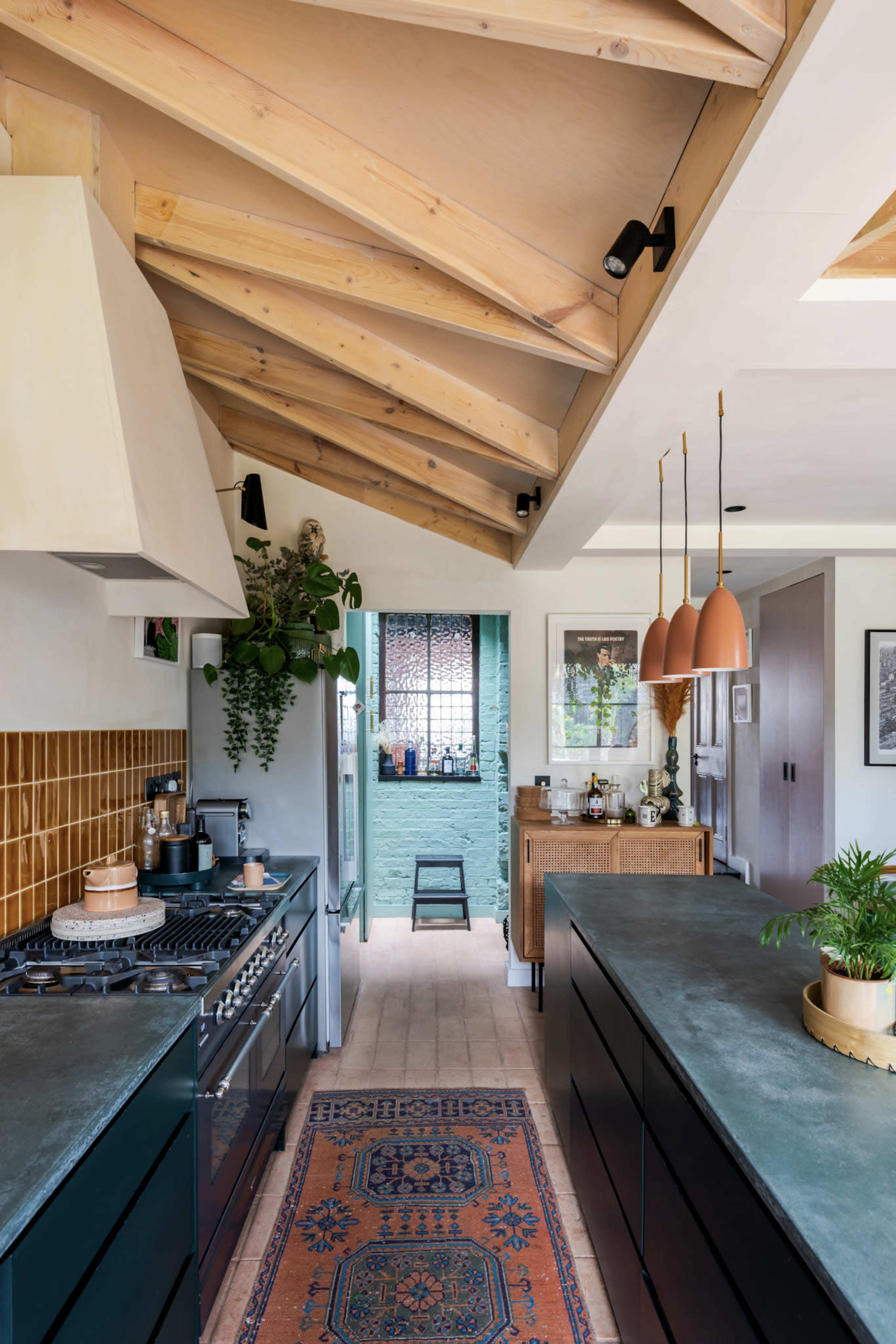 A modern kitchen features a wooden ceiling with exposed beams, a central island, and a cozy dining area in the background.