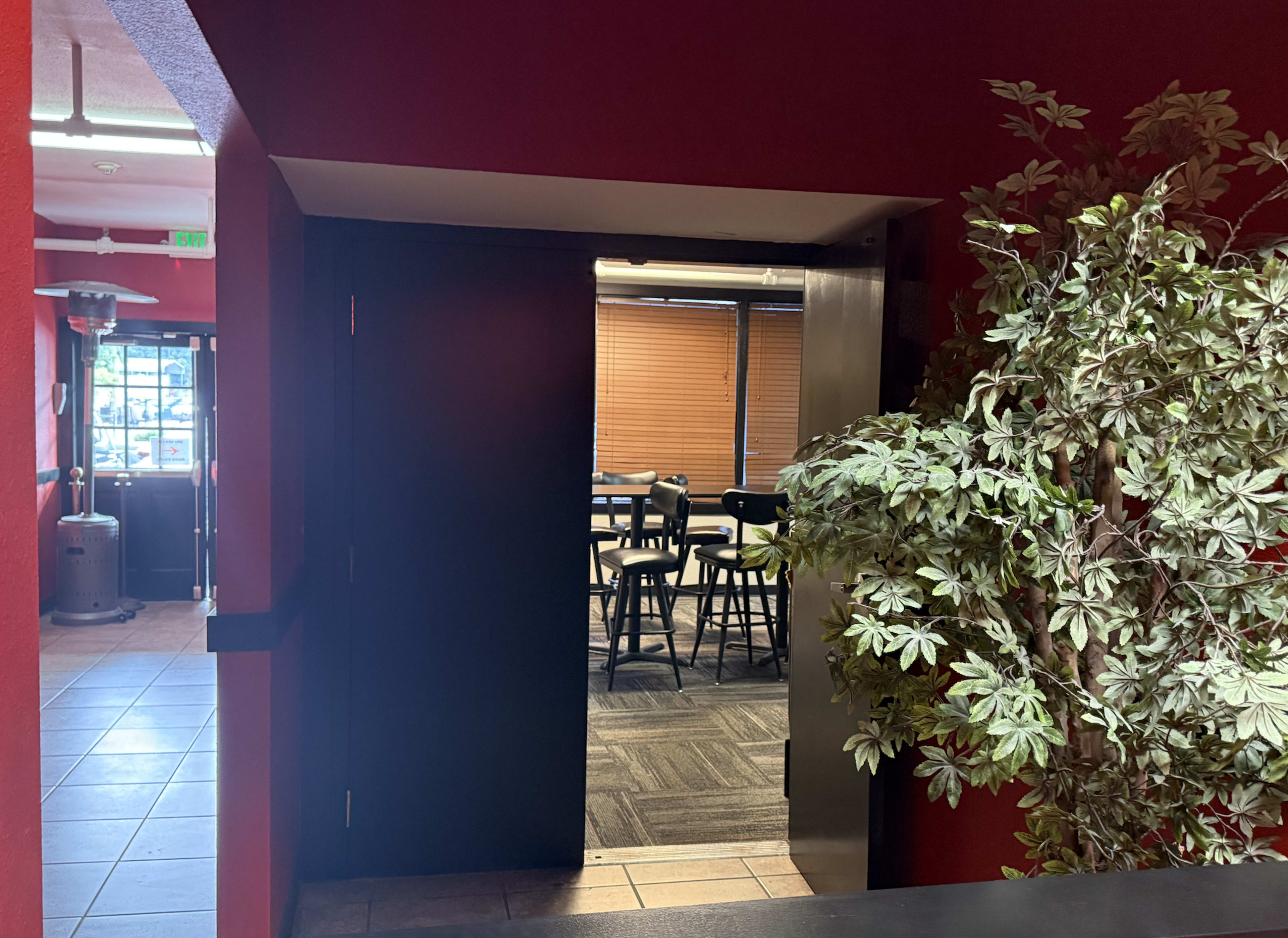 A doorway leads into a room with tables and chairs, framed by a potted plant on the side.