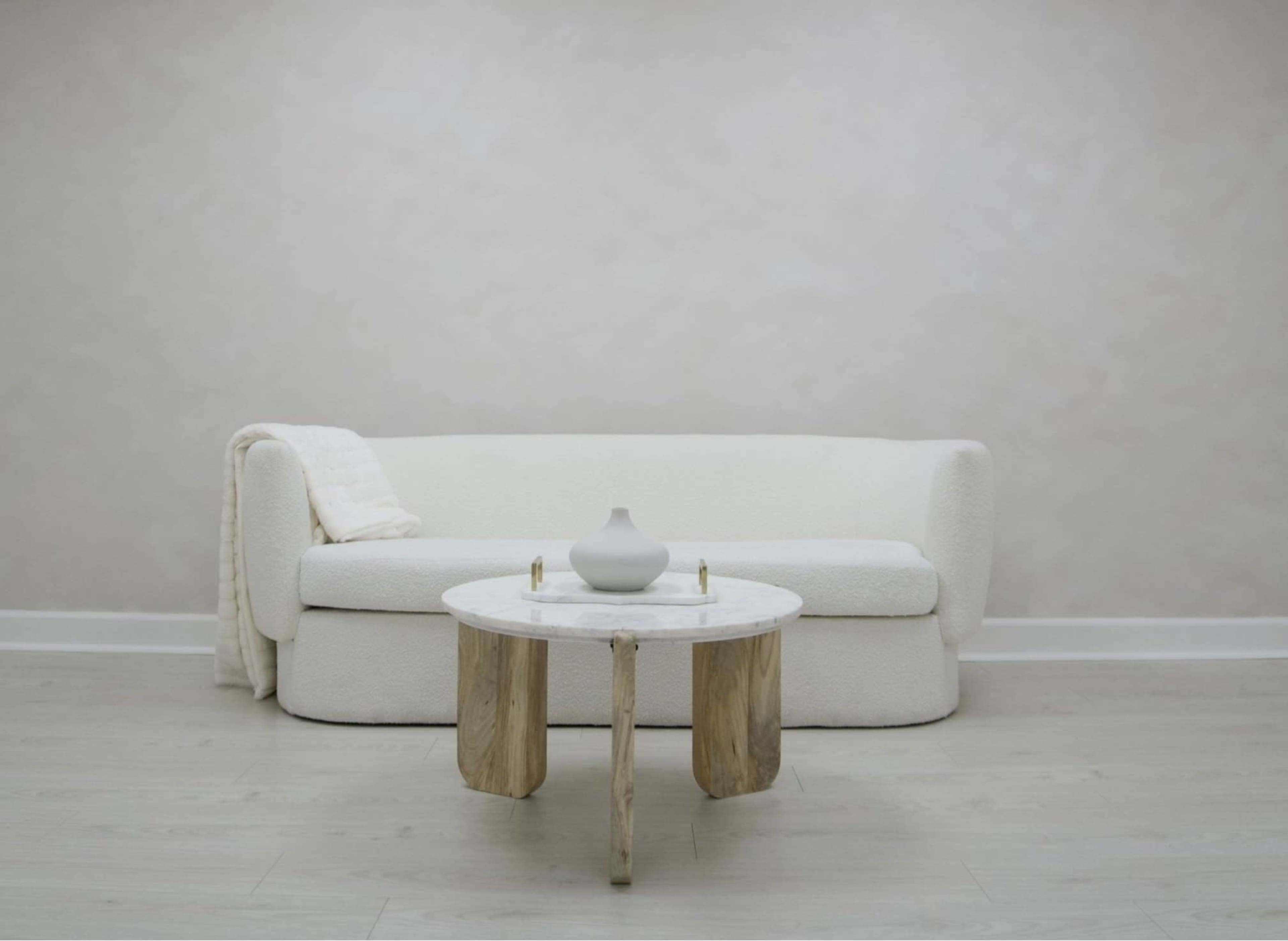 A white, upholstered sofa sits facing a round coffee table made of marble and wood in a minimalist interior space.