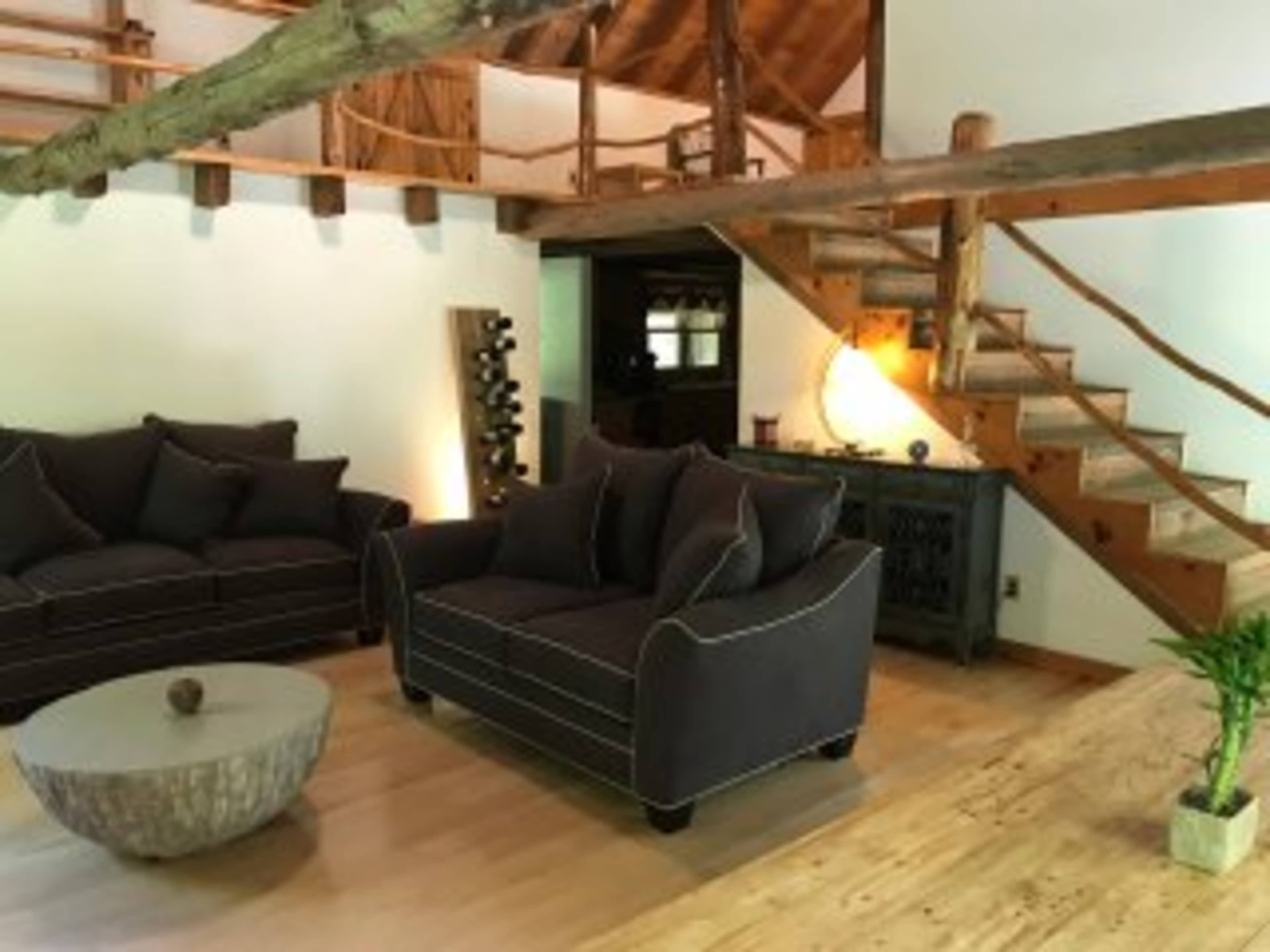 A cozy living room featuring two dark sofas, a round wooden coffee table, and a staircase leading to an upper level.