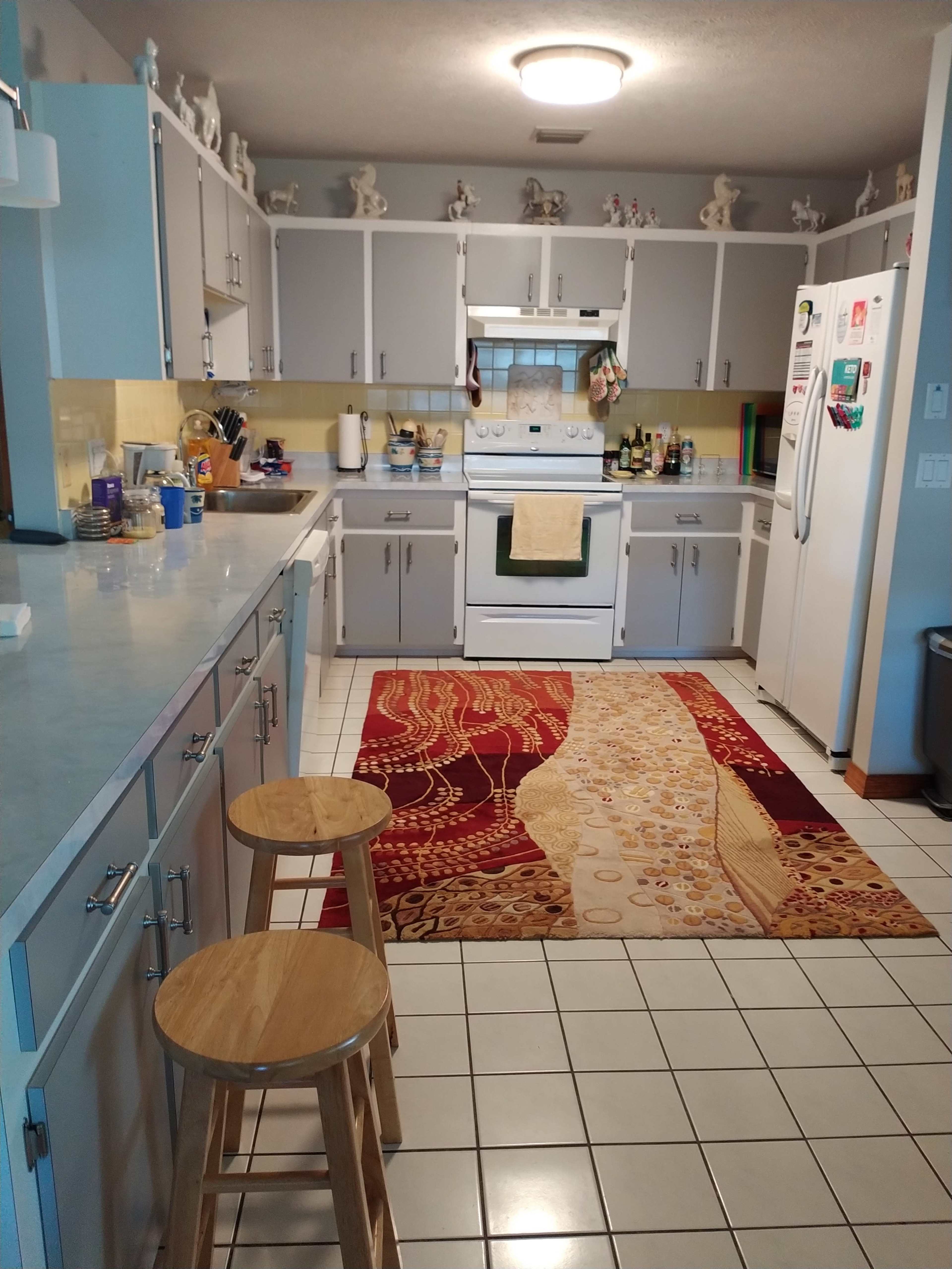 A kitchen featuring light gray cabinets, a white stove and refrigerator, and a patterned area rug on the tiled floor.