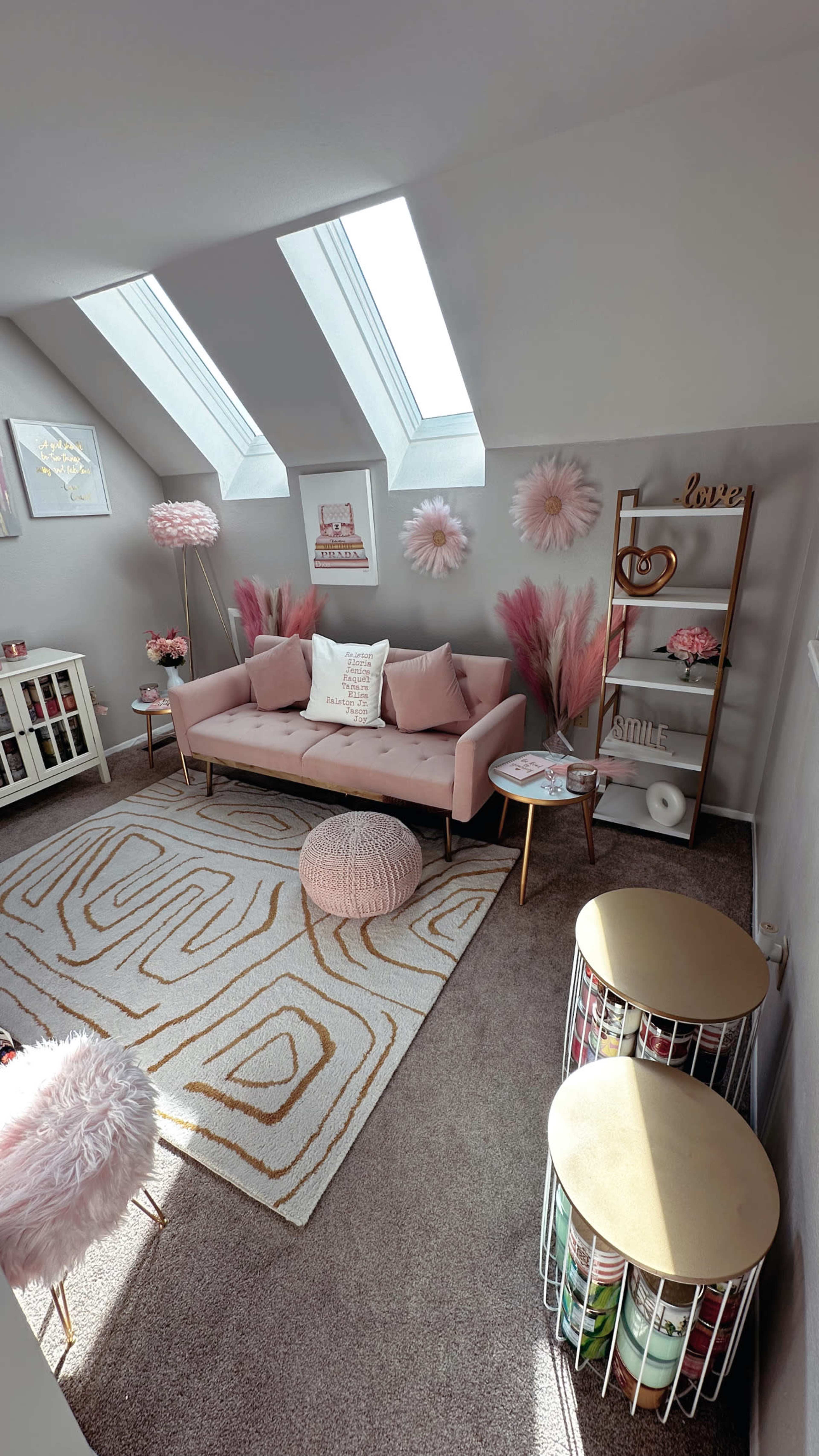 The image shows a cozy, well-decorated room featuring a pink couch, decorative plants, art on the walls, and contemporary furniture.