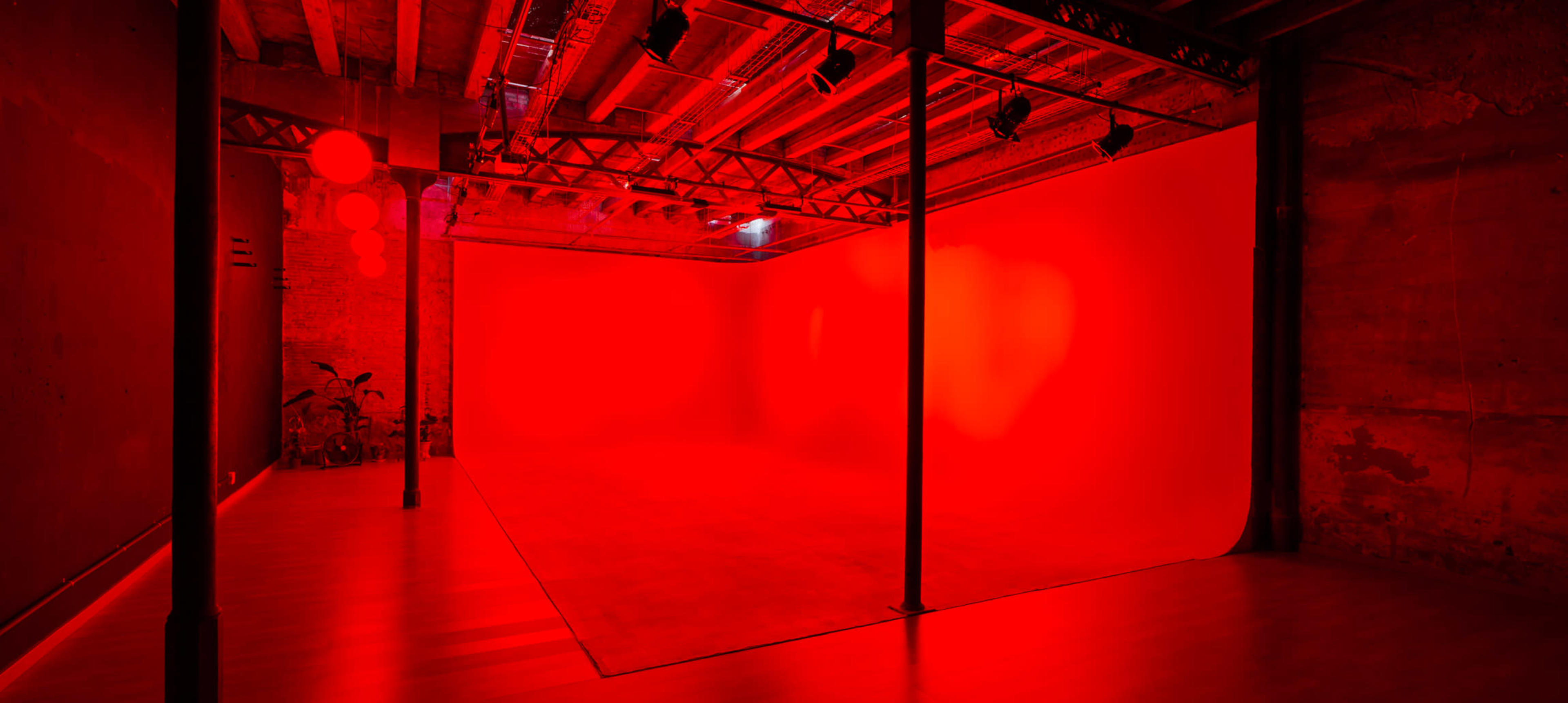 A spacious studio with a red backdrop and exposed beams, illuminated by red lighting.
