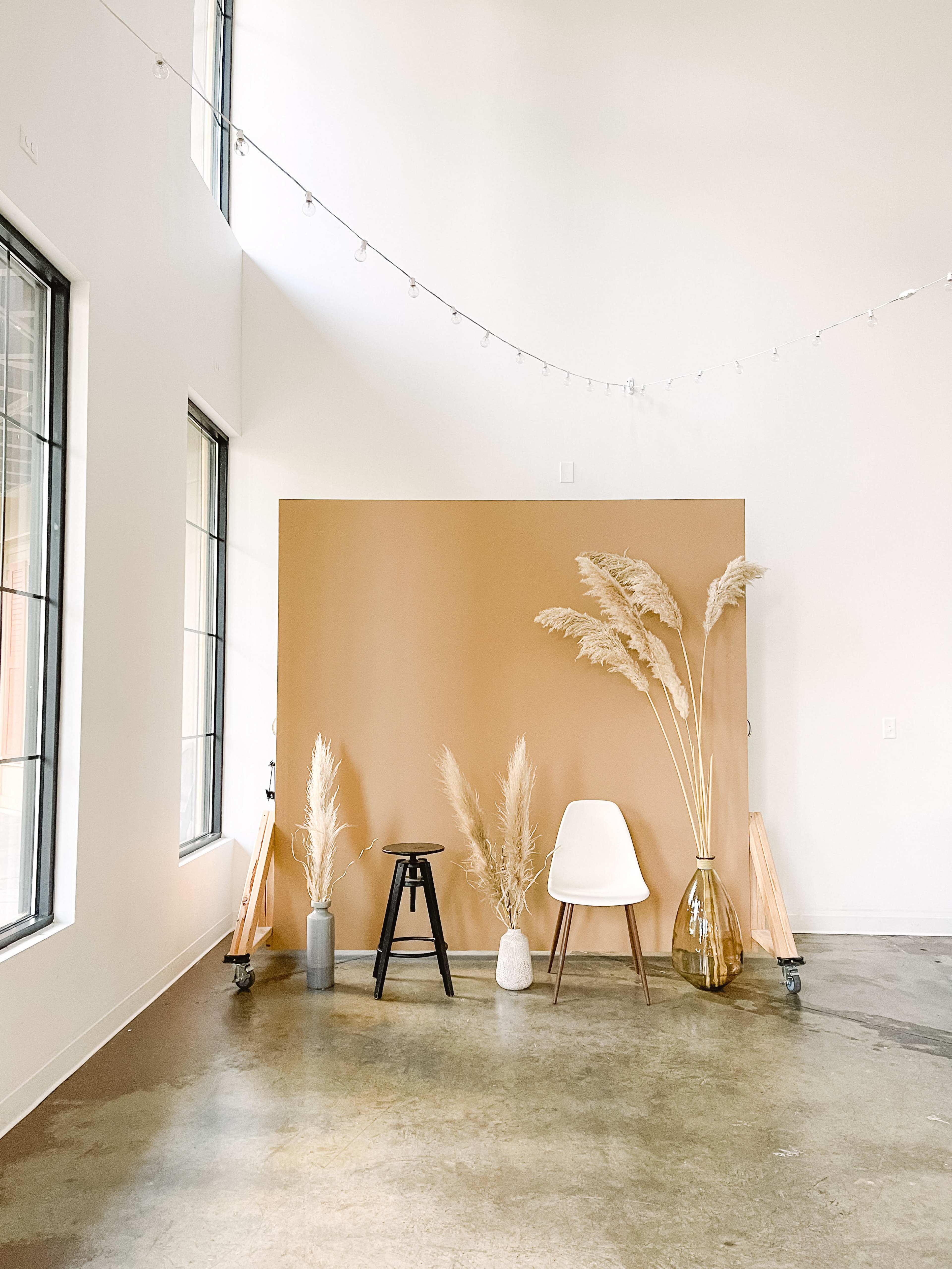 A serene indoor space featuring a brown backdrop flanked by decorative vases and plants, including a white chair and a black stool.