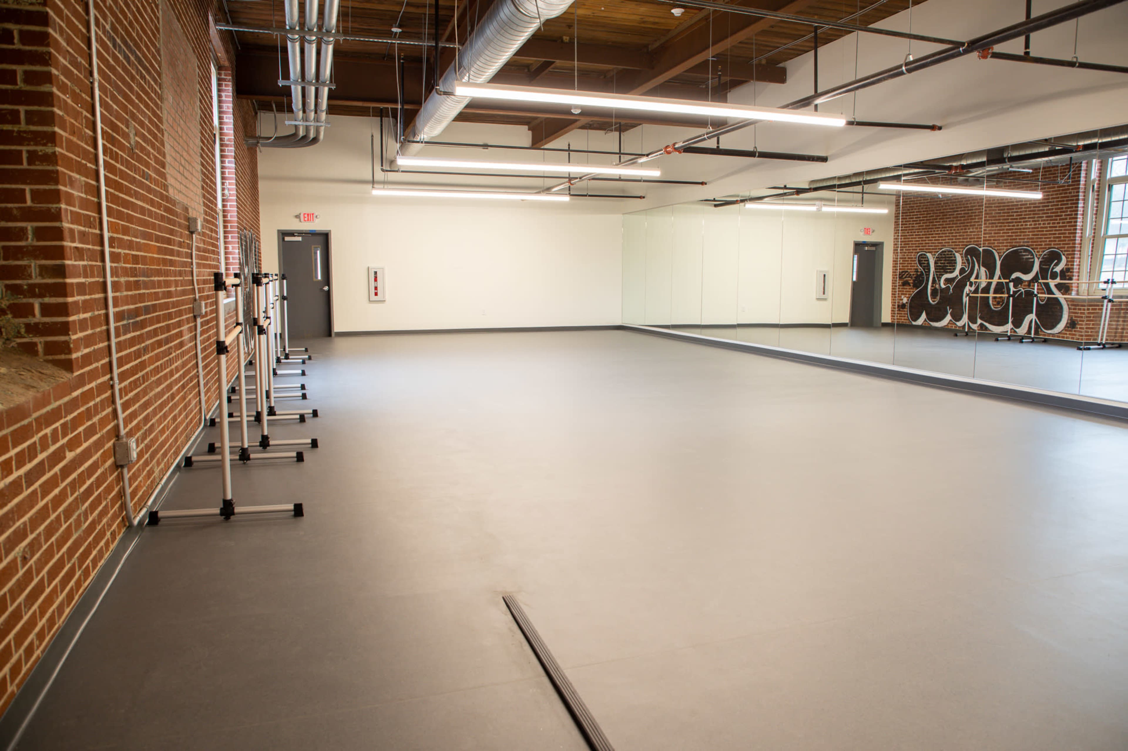 An empty dance studio with mirrored walls, a smooth floor, and brick accents.