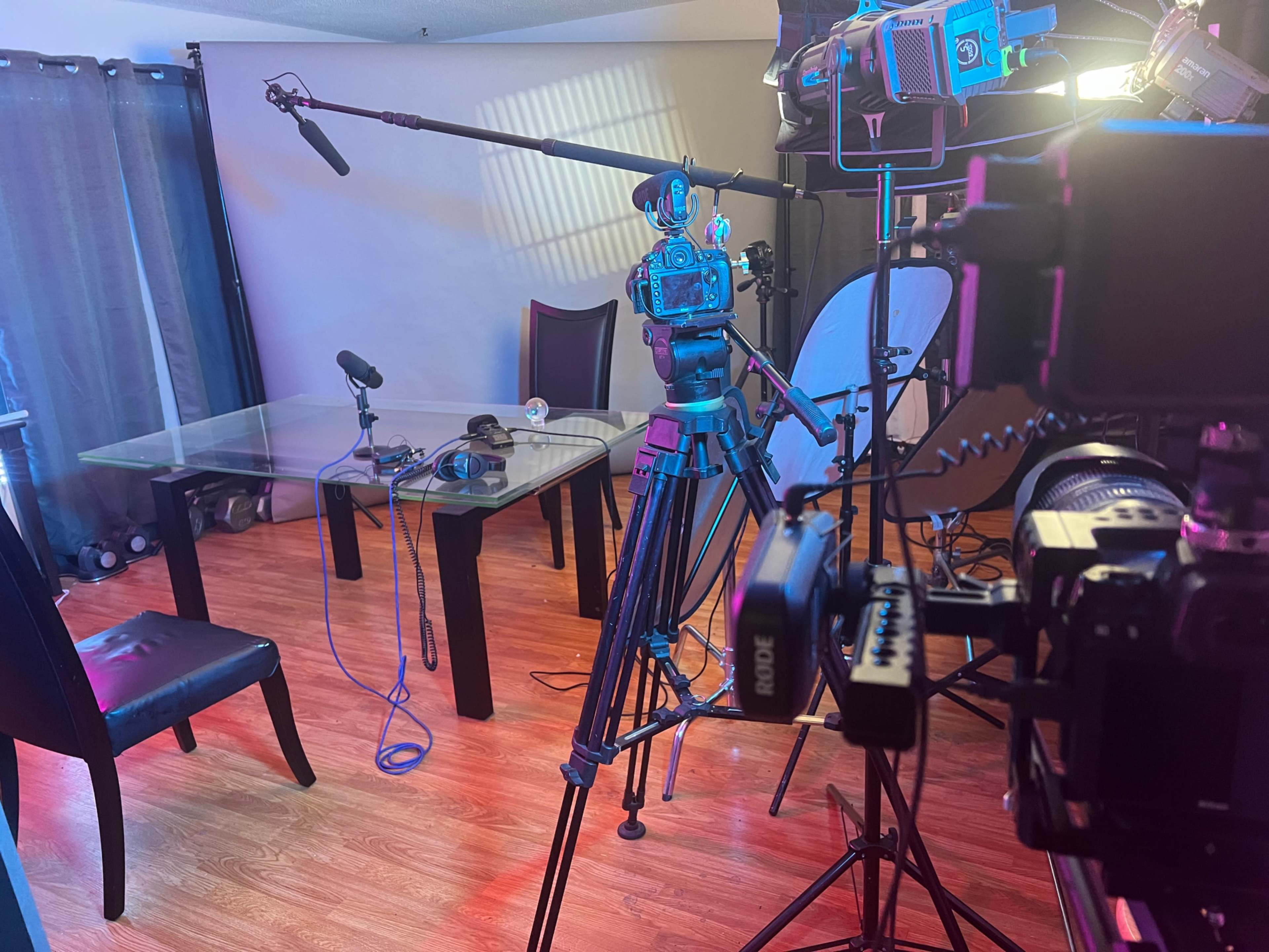 A well-equipped recording studio with a glass table, microphones, and several cameras positioned on tripods.