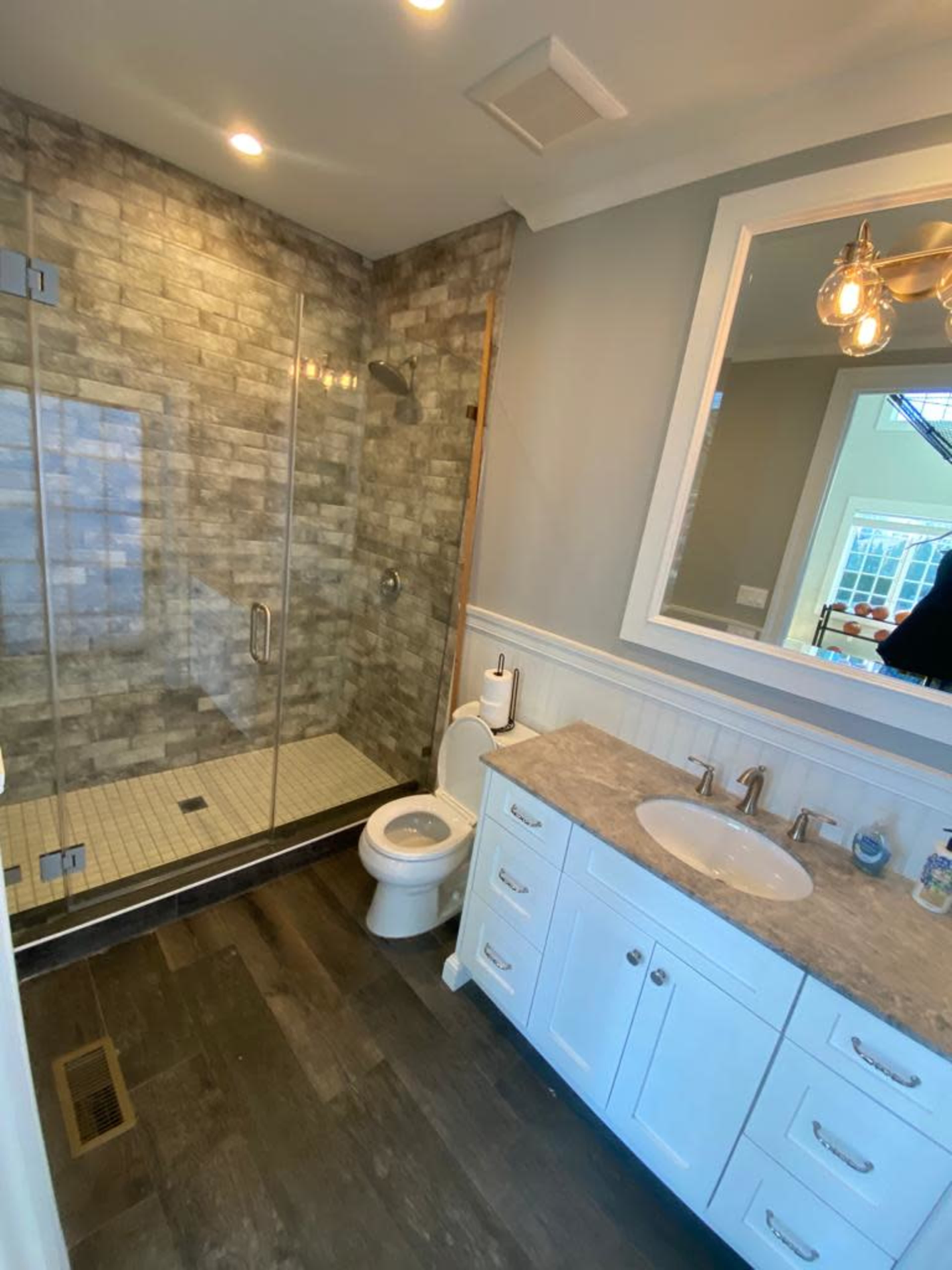 The image shows a modern bathroom featuring a glass shower, a toilet, and a double sink vanity with a marble countertop.