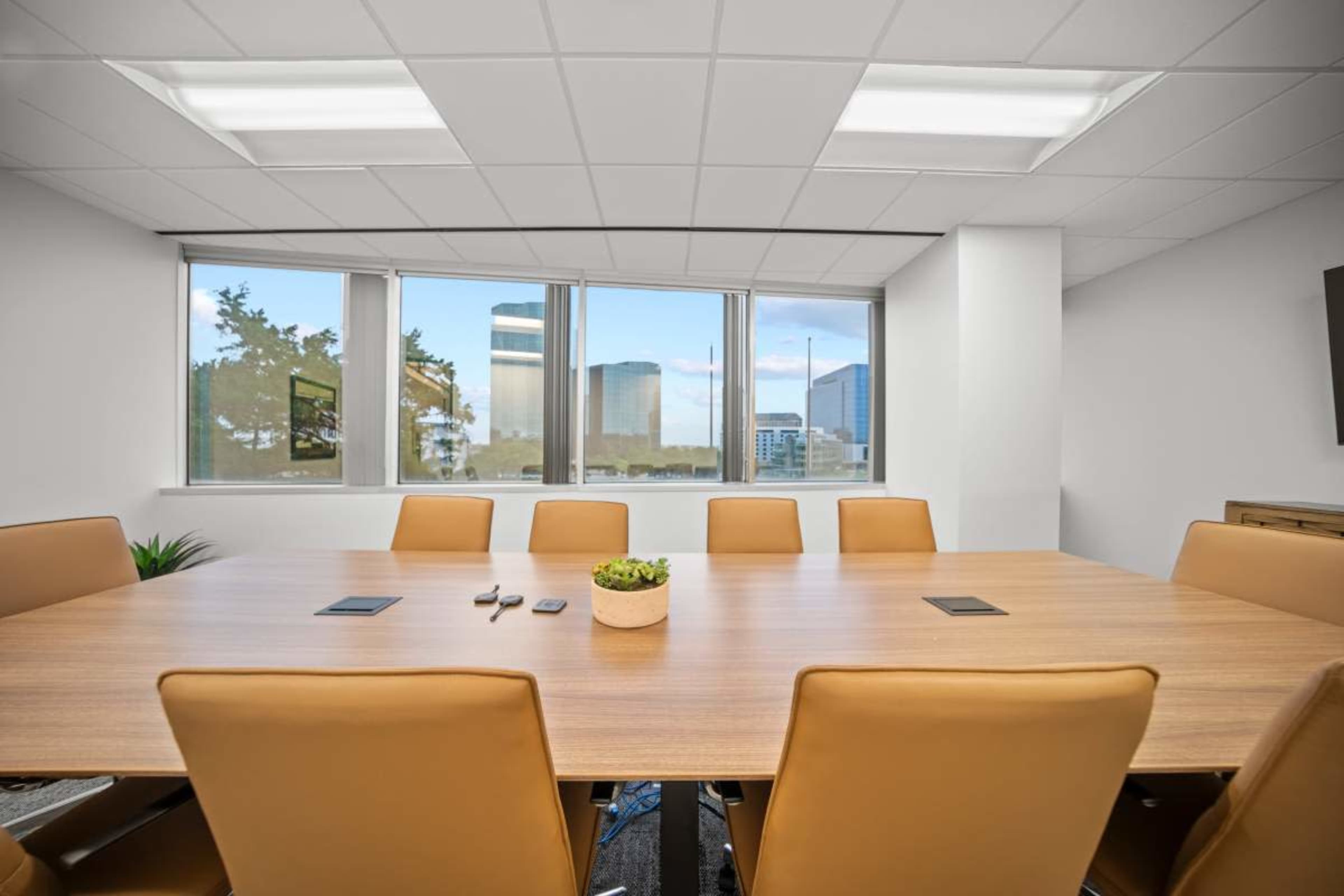 A large conference room features a wooden table surrounded by brown leather chairs and large windows displaying a city skyline.