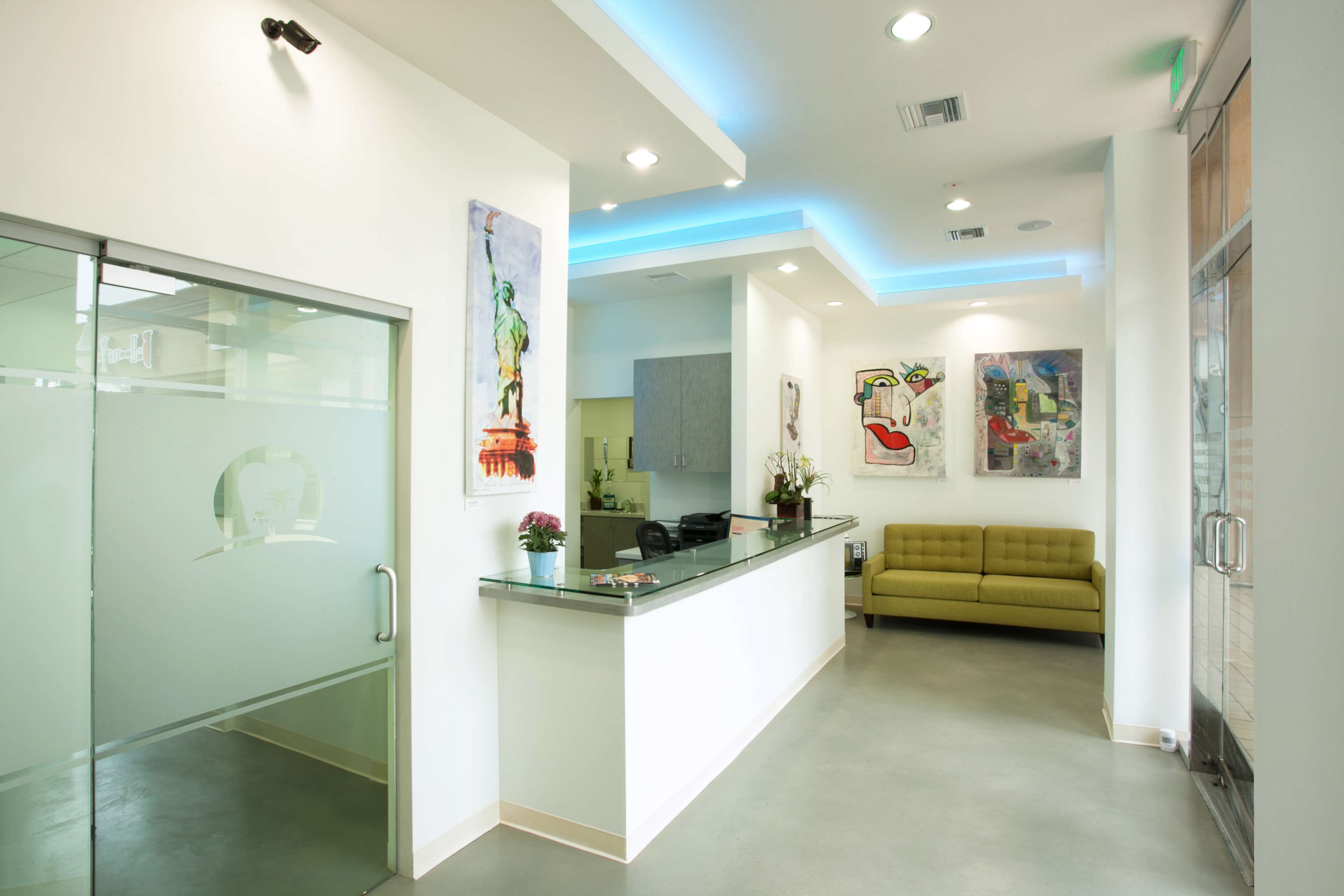 The image shows a modern reception area with a glass door, a front desk, a green couch, and colorful artworks on the walls.