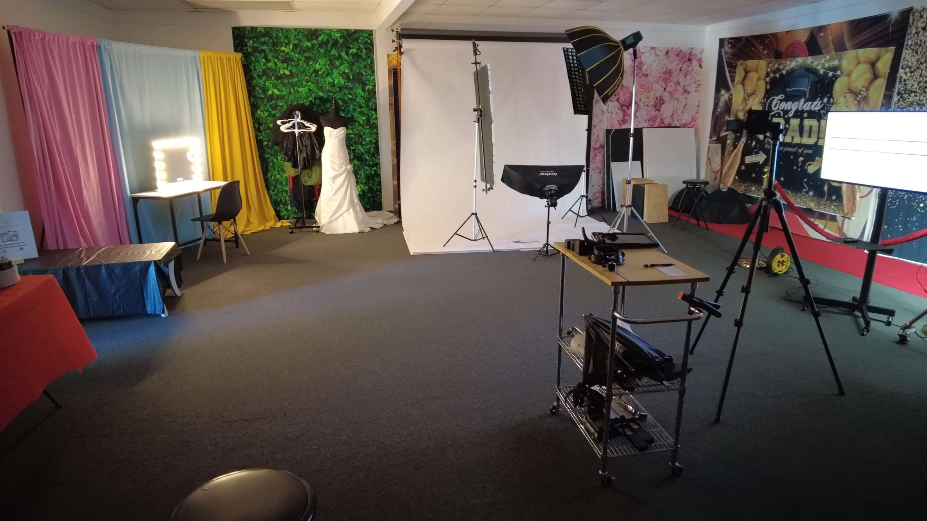 A photography studio is set up with a backdrop, lighting equipment, and a dressing area featuring a wedding dress on a hanger.